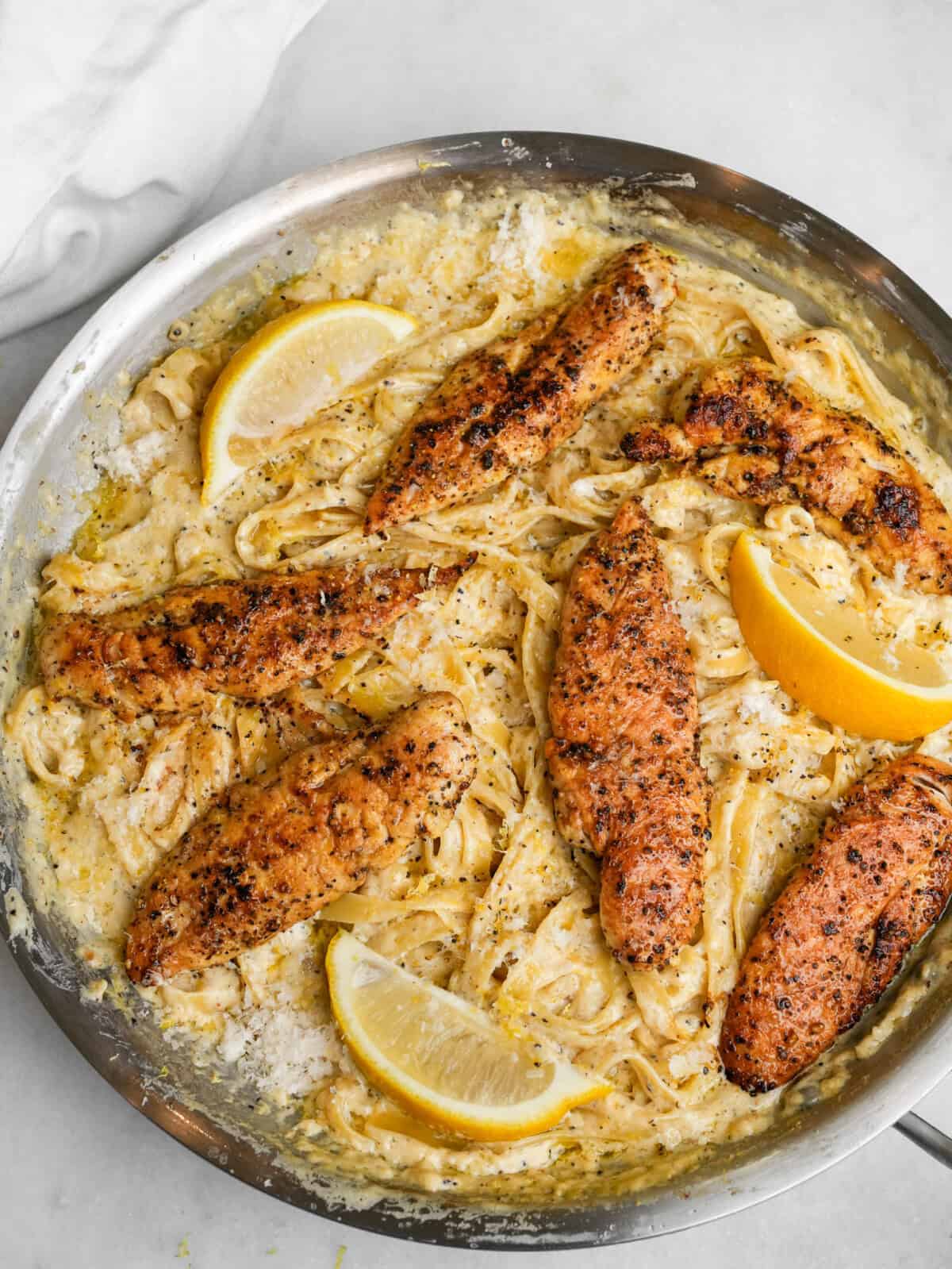 lemon pepper chicken on fettuccine alfredo in a pan