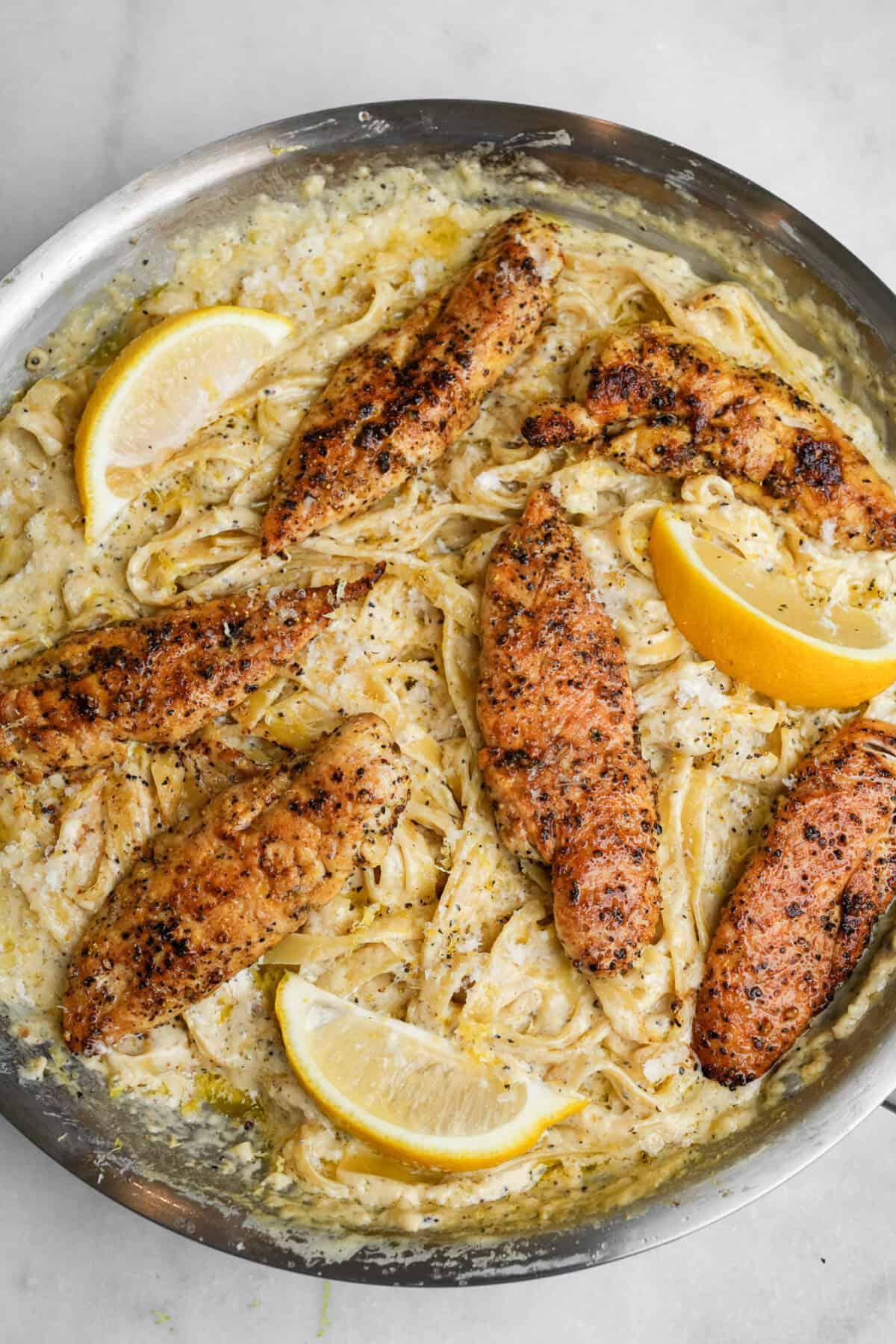 lemon pepper chicken on fettuccine alfredo in a pan