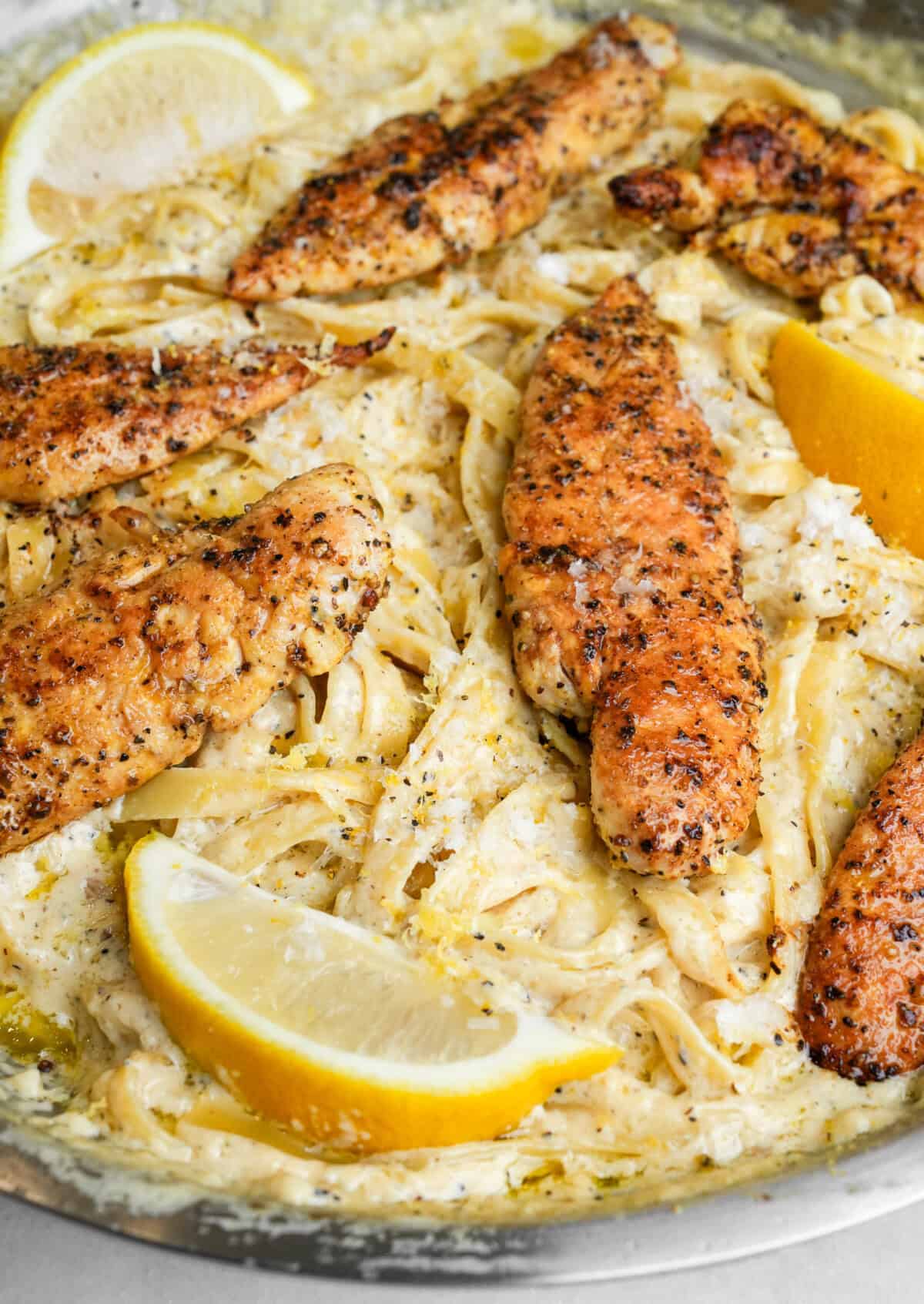 lemon pepper chicken on fettuccine alfredo in a pan