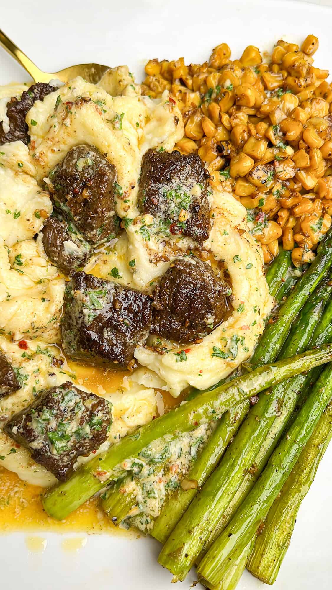 dinner plate with potatoes, steak, asparagus and corn drizzled with cowboy butter