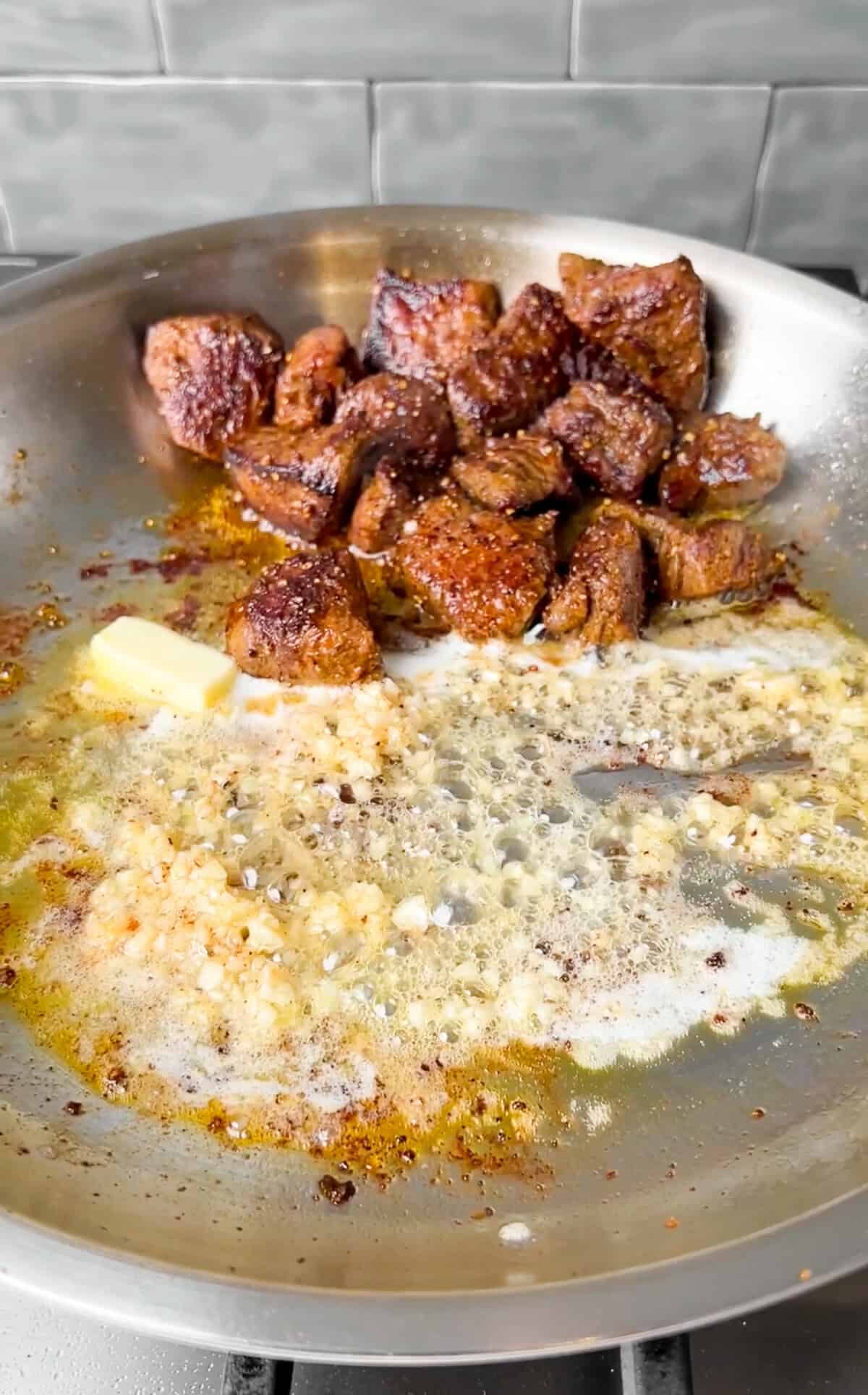 steak bites being tossed in garlic butter in a pan