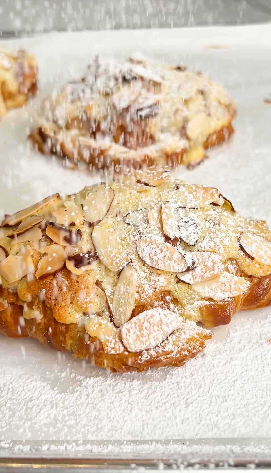 dusting almond croissants with powdered sugar