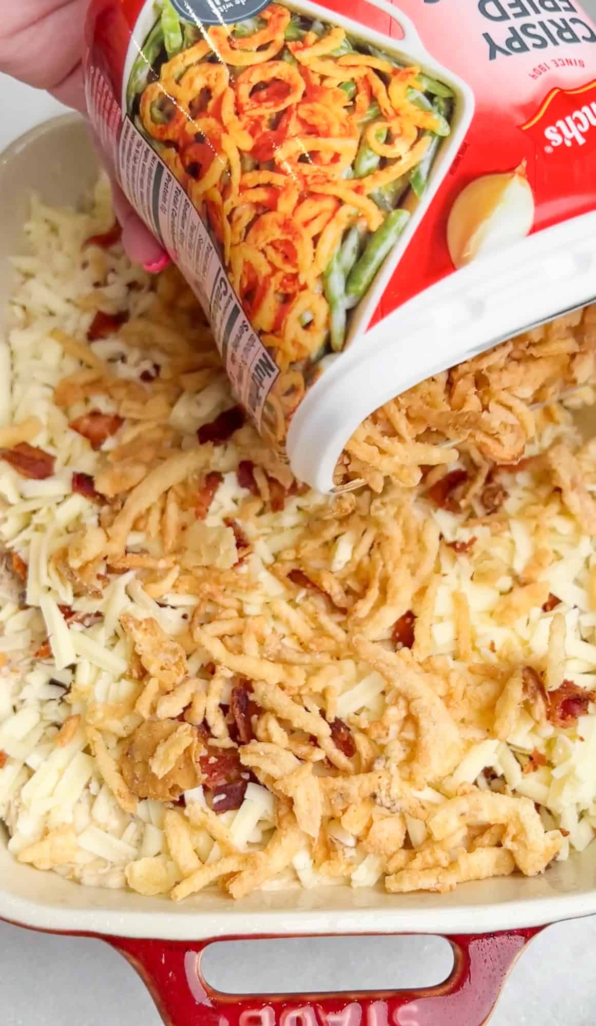 pouring french fried onions over the dip in a pan