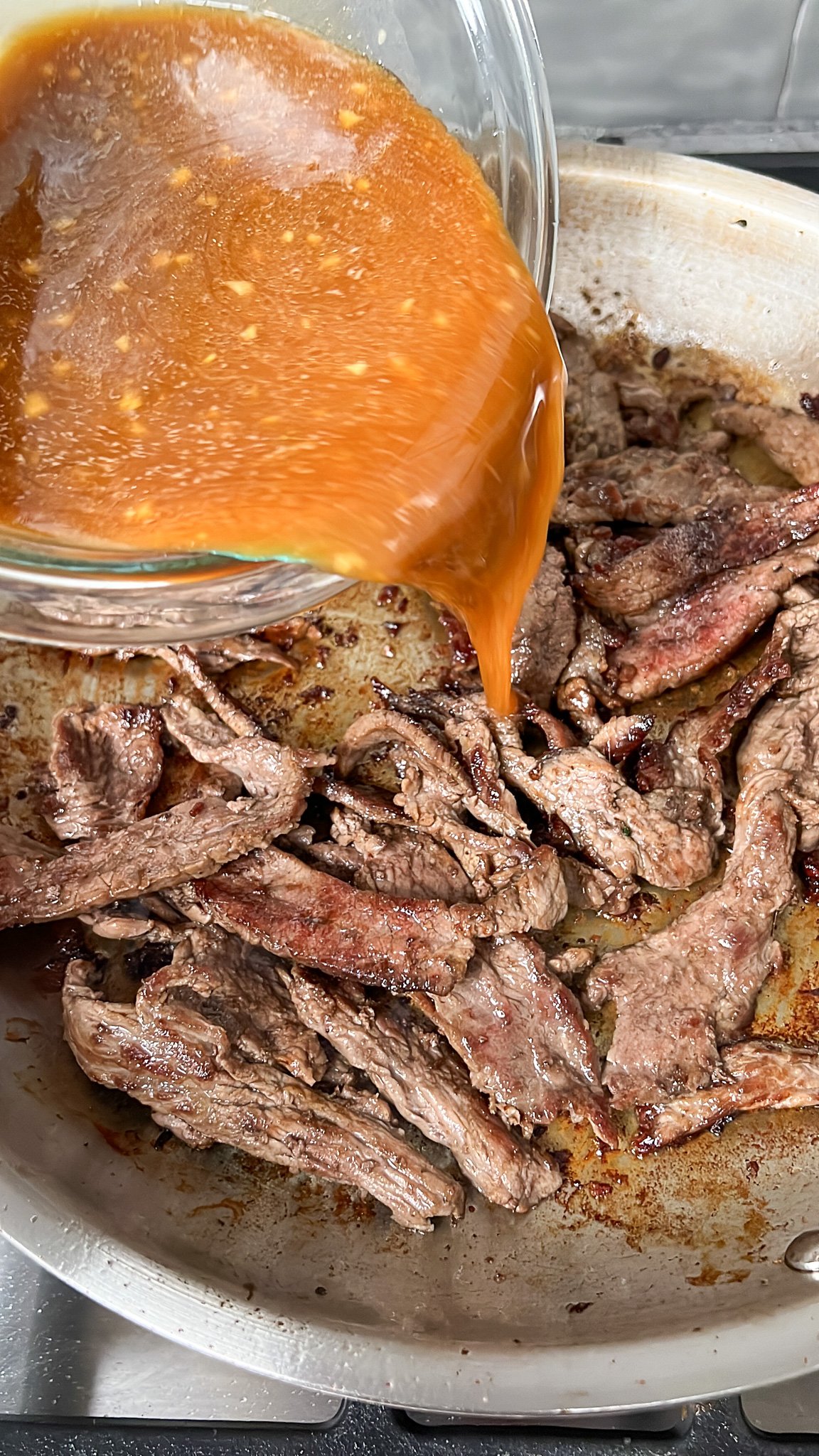 sauce pouring into the pan of beef