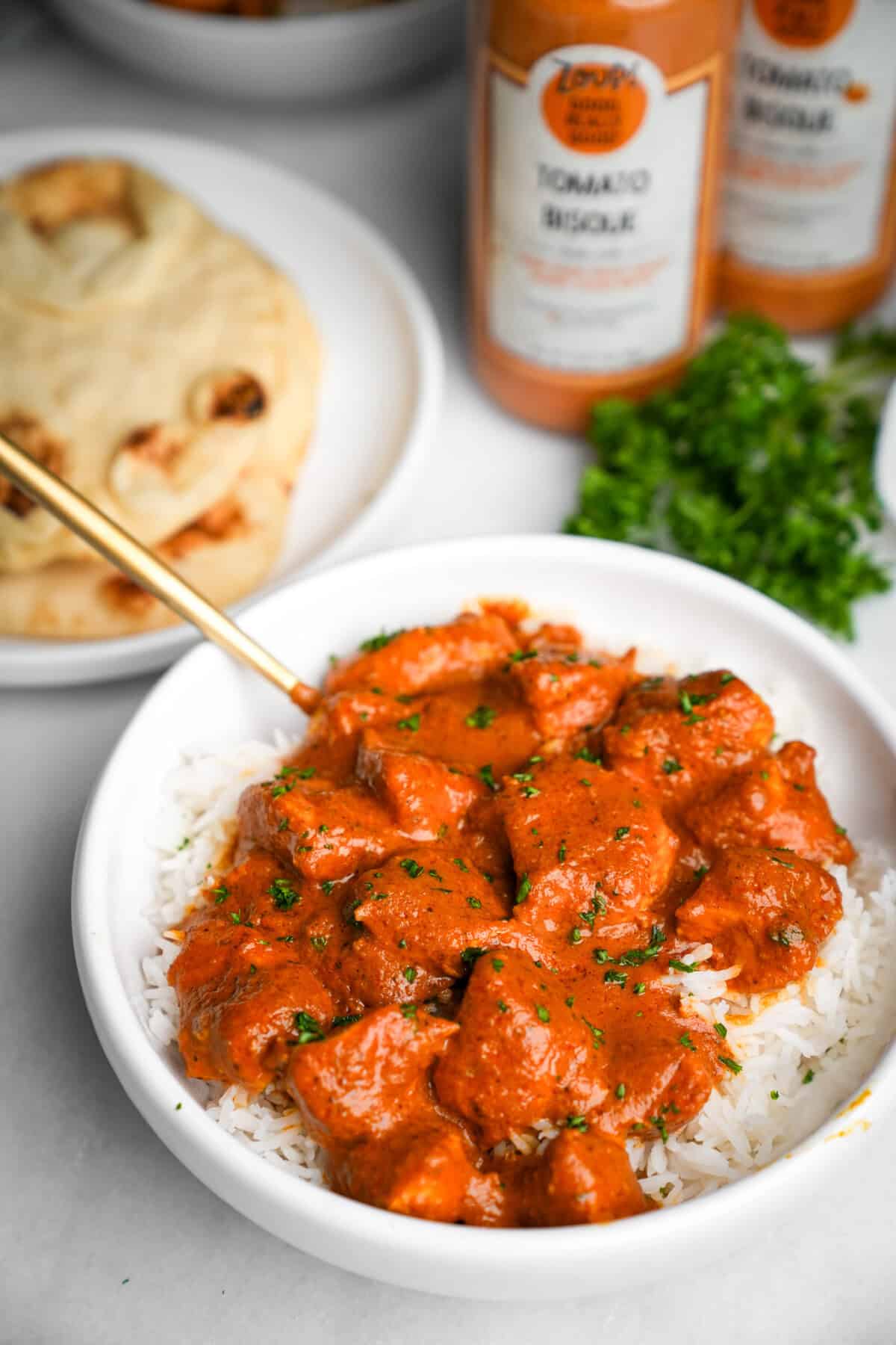 butter chicken in a bowl over rice next to naan bread