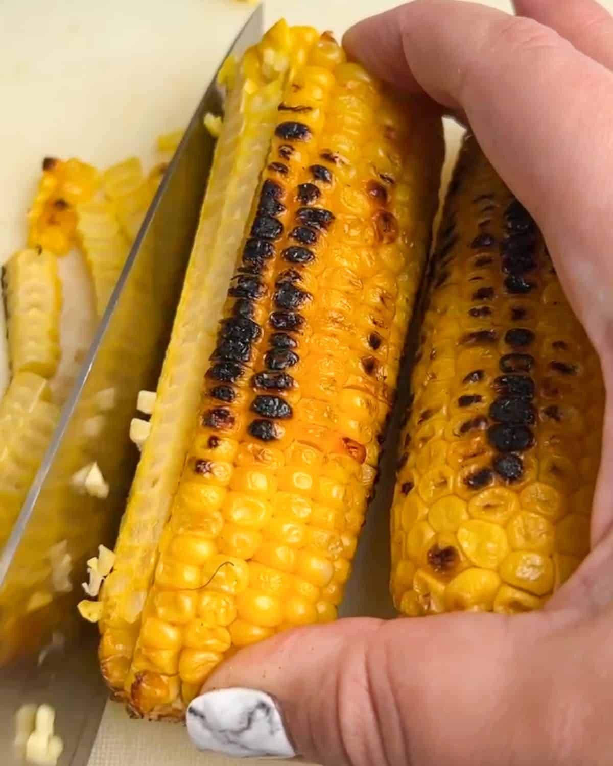 With sautéed corn, peppers, onion, and lots of cheese, this Baked Hot Corn Dip is creamy, cheesy, and packed with flavor. A knife slicing corn kernels off the cob