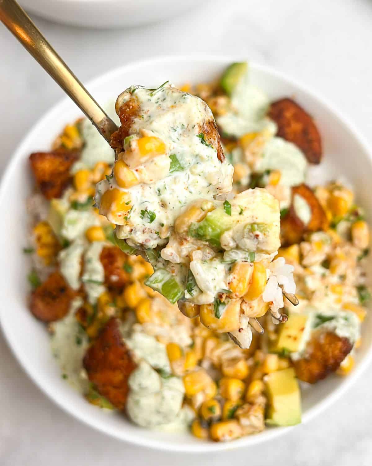 a bowl with street corn and chicken on a spoon