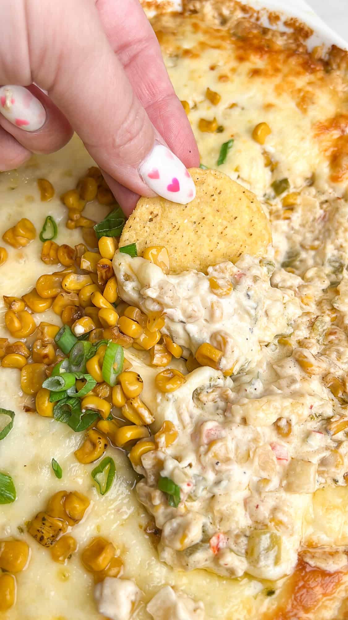 hot corn dip in a casserole dish digging in with a tortilla chip