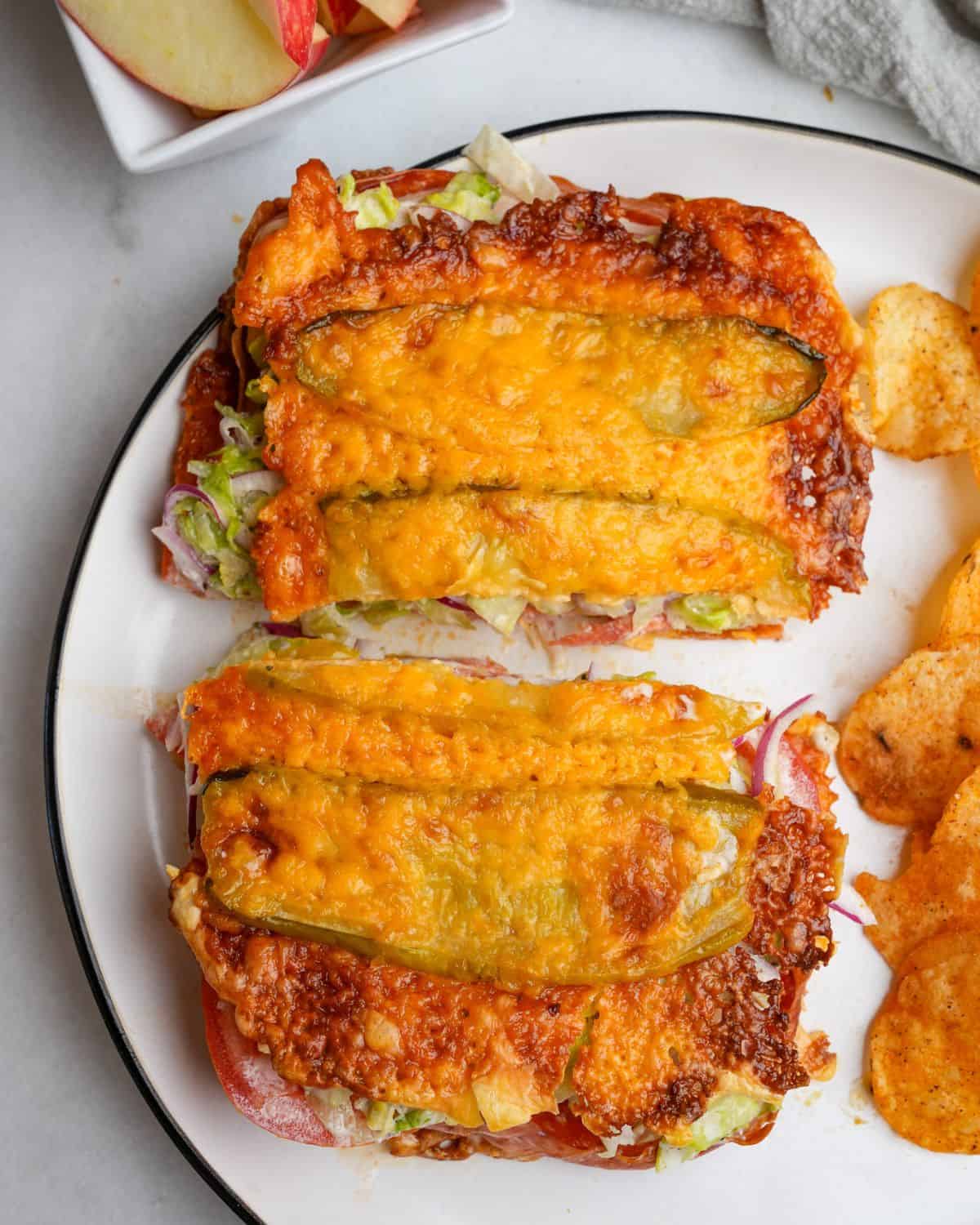 Thinly sliced pickles and shredded cheese are baked together to make a low-carb “bread” in this viral pickle sandwich recipe. A viral pickle sandwich on a plate cut in half