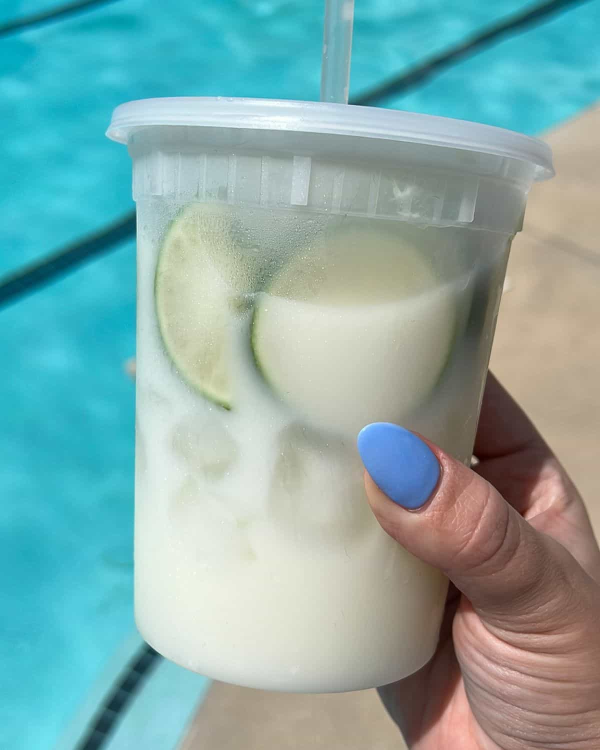 A hand holding a cup of Brazilian limeade by the pool.