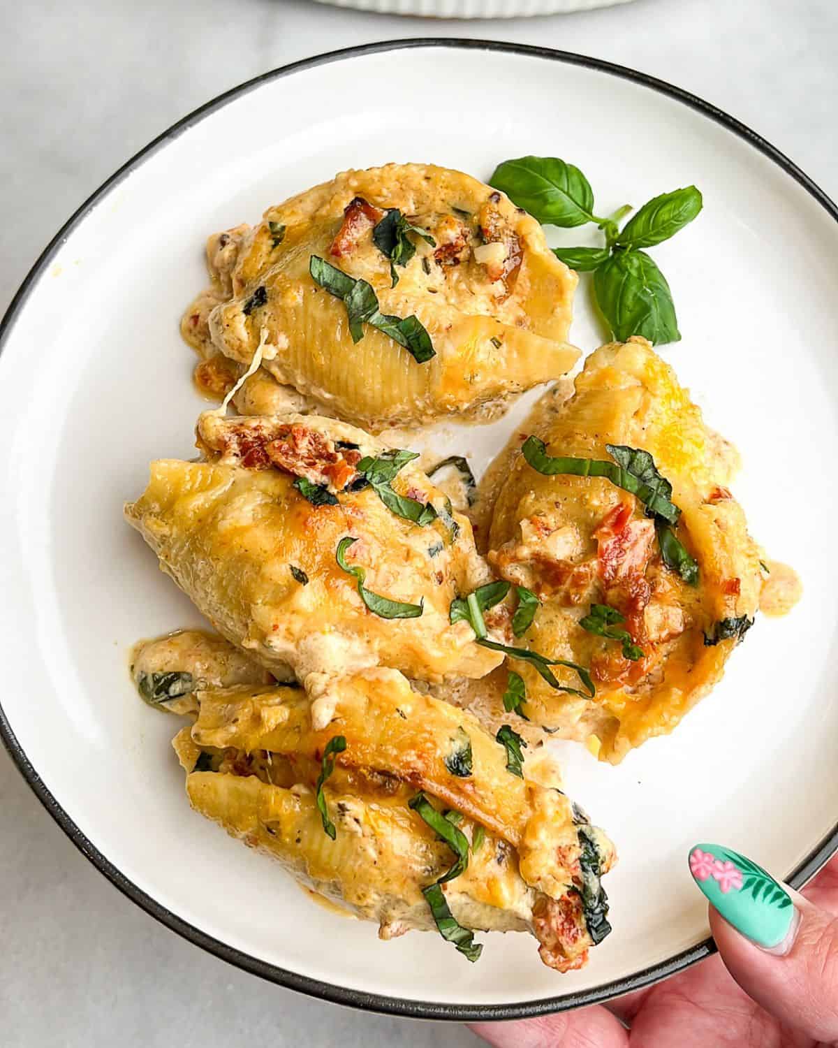 A hand holding a plate of marry me chicken stuffed shells.