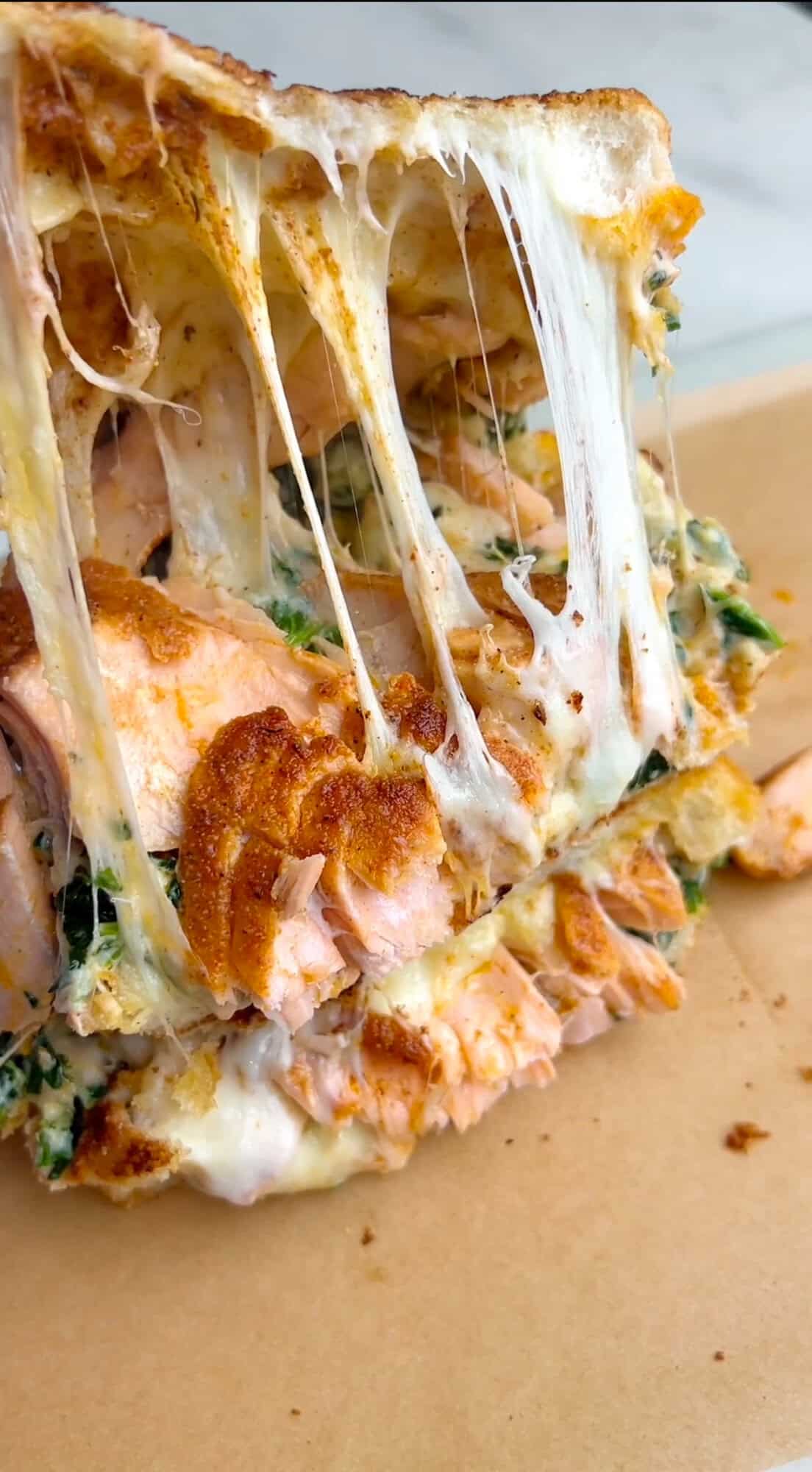 Lifting the top piece of bread from a salmon grilled cheese sandwich to reveal the inside.