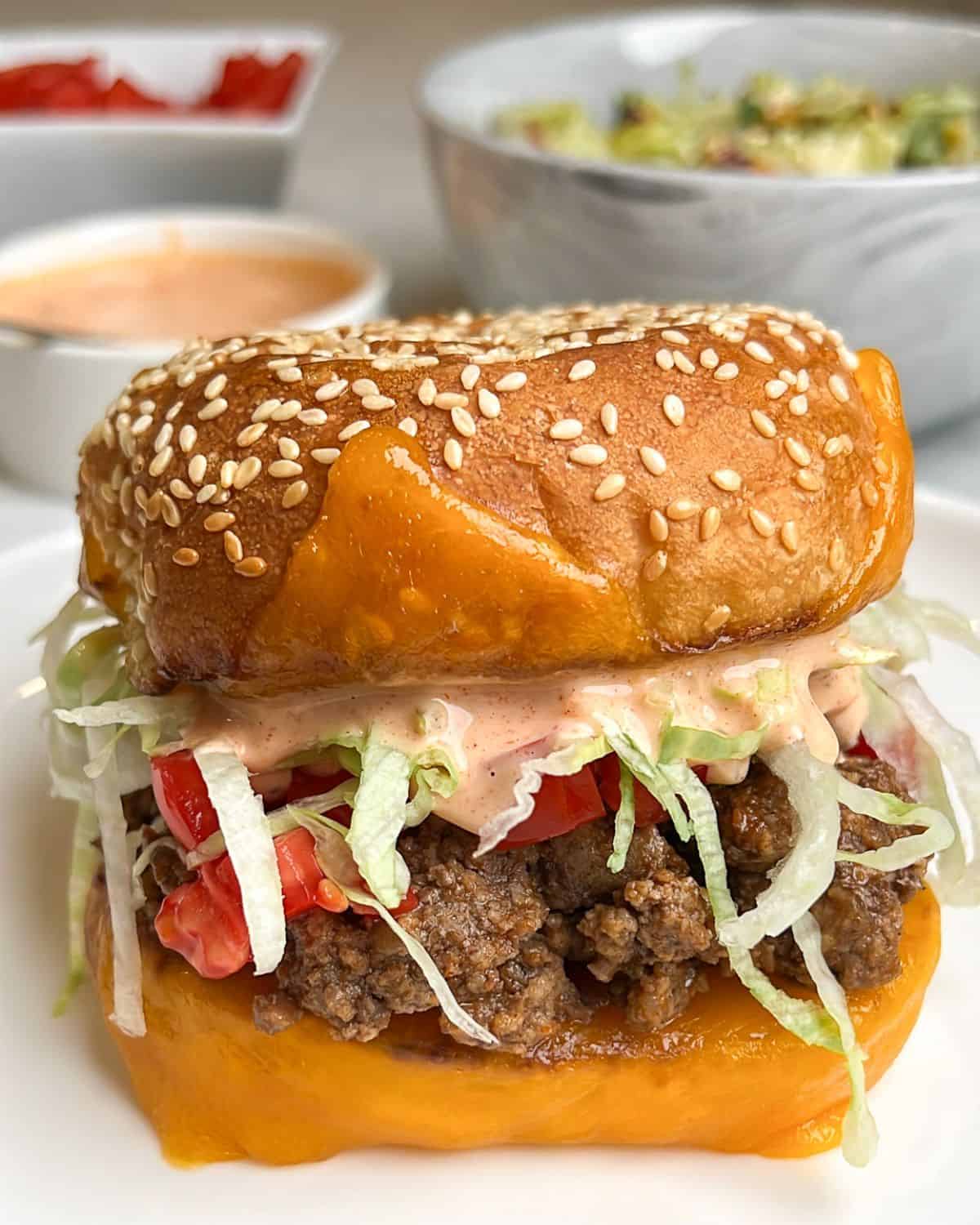 A taco burger with thousand island dressing and a bowl of slaw in the background.