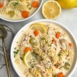 Two bowls of creamy chicken noodle soup with lemon wedges.