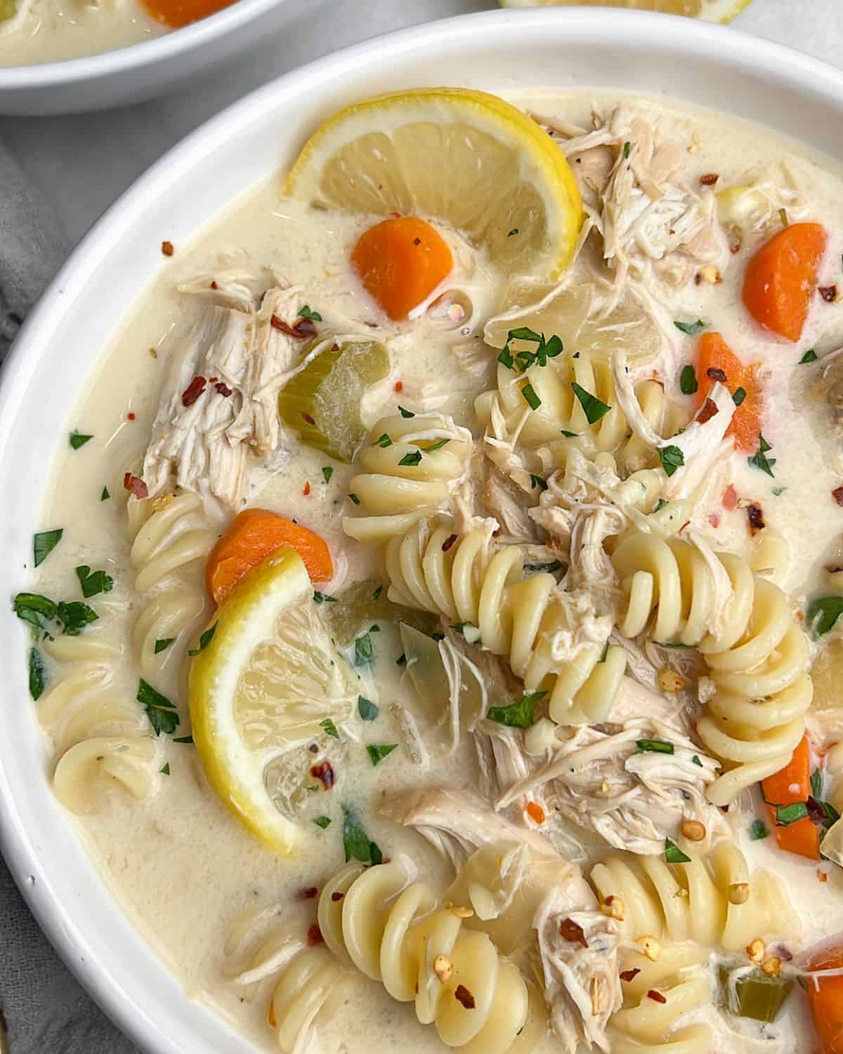 Slow-cooker creamy chicken noodle soup is finished with cream, Parmesan, and fresh lemon. It's a fun spin on a classic comfort food fave. Close-up image of a bowl of creamy chicken noodle soup.