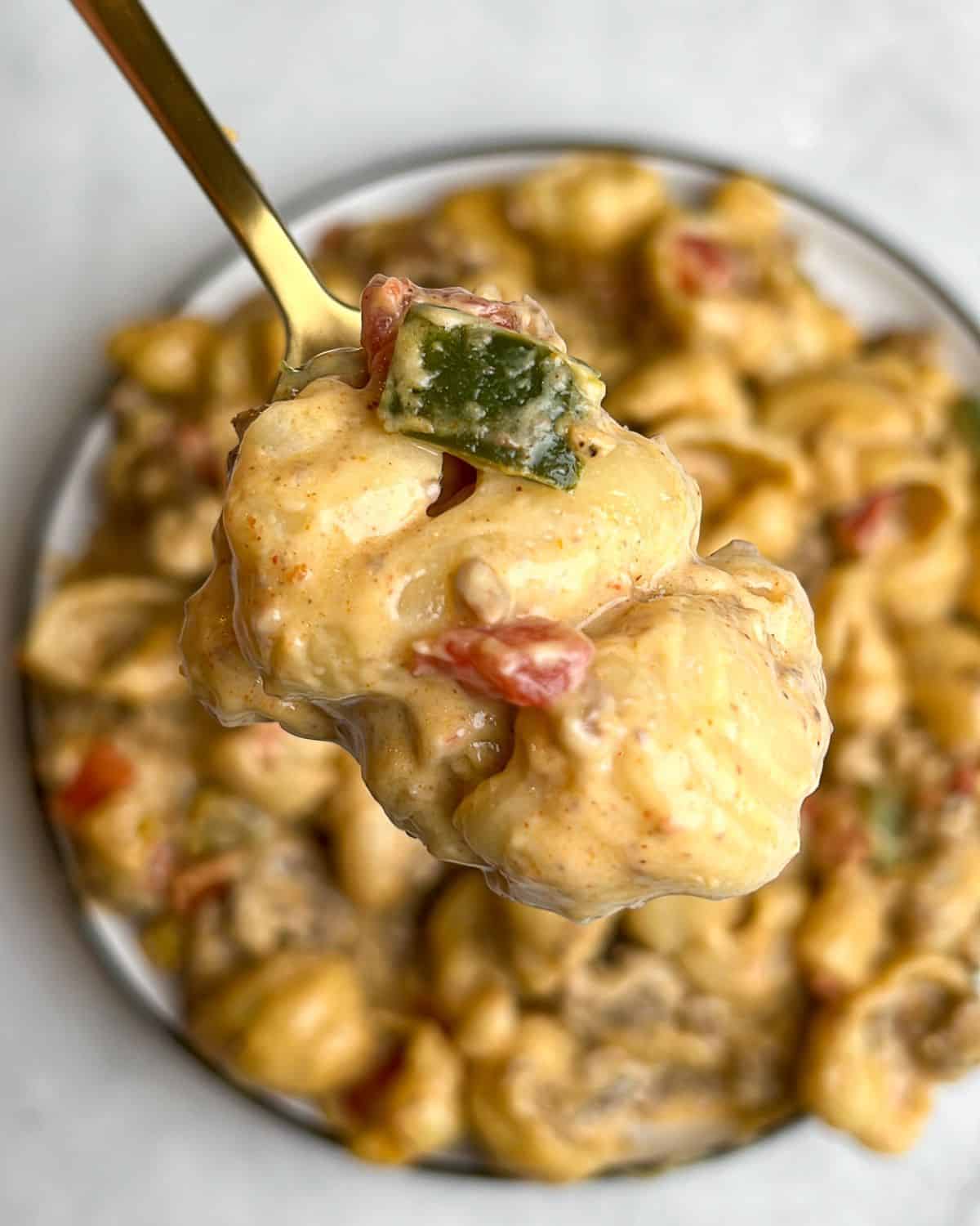 A spoon holding a bite of taco mac and cheese up to the camera.