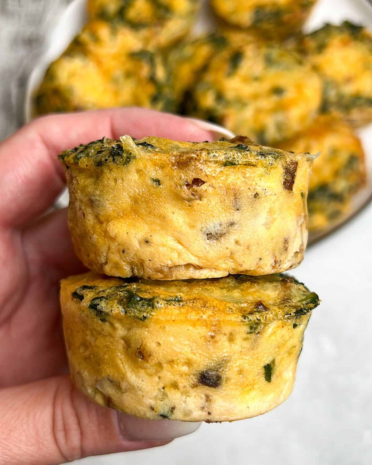A hand holding a 2 kale and mushroom egg bites up to the camera.