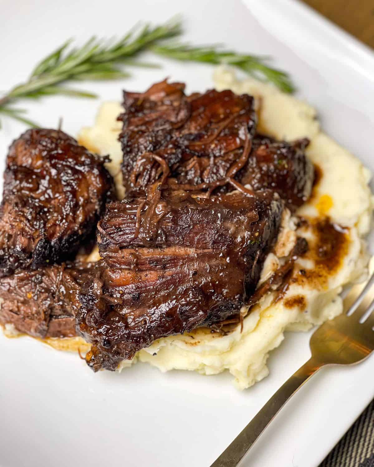 Craving a cozy meal? This red wine pot roast is it! With tender meat and rich flavors, it’s an indulgent dish made for chilly nights. Red wine pot roast over mashed potatoes with a sprig of rosemary.