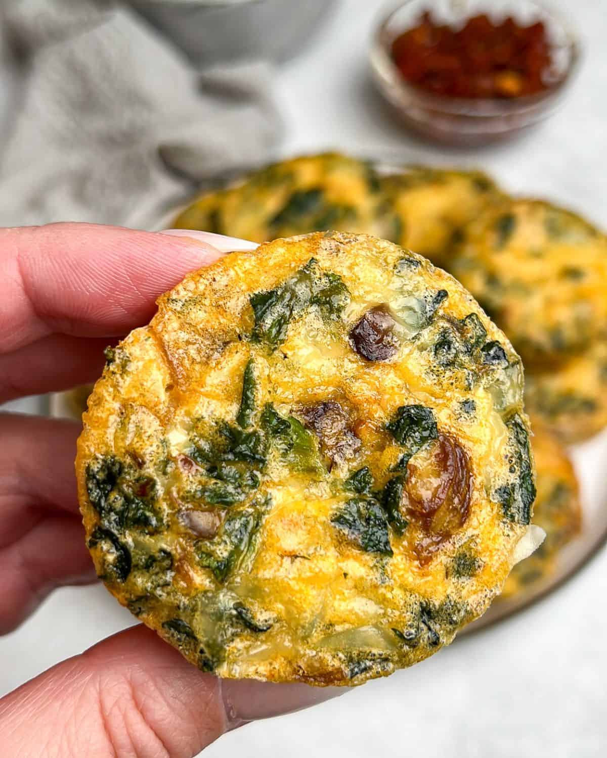 A hand holding a kale and mushroom egg bite up to the camera.