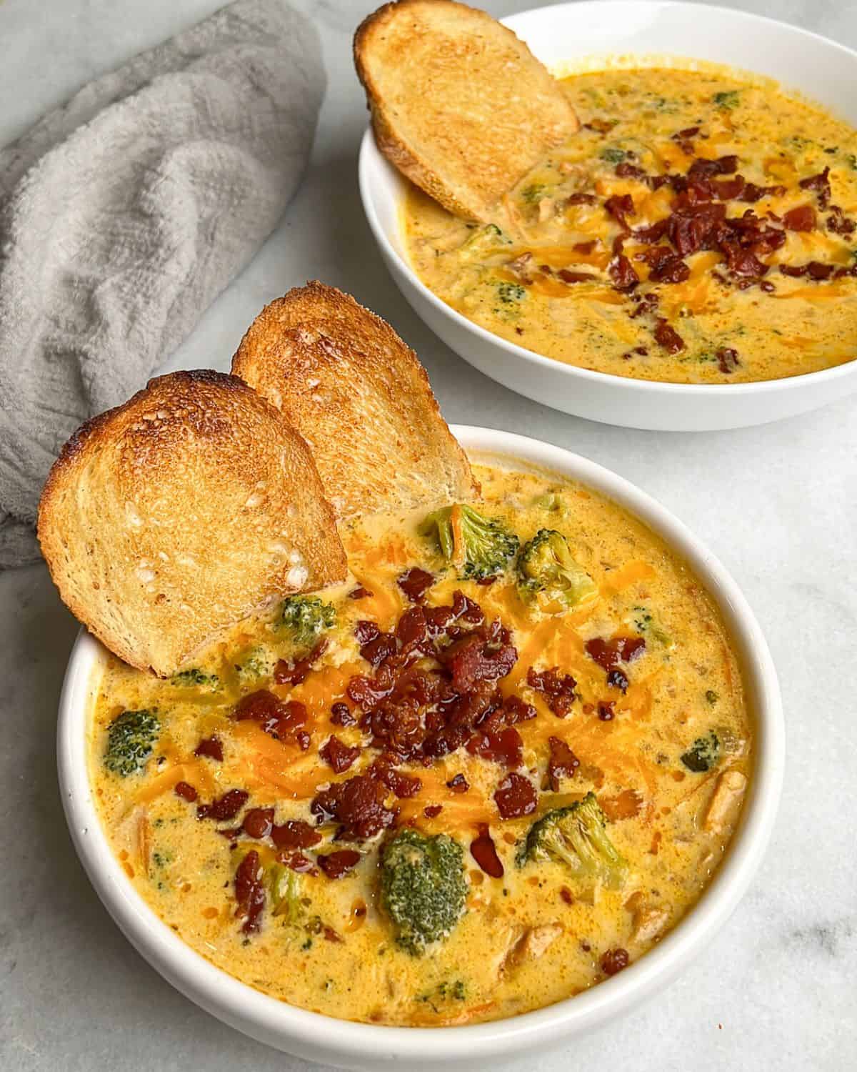 two bowls of cheesy broccoli soup in a bowl with buttered toast