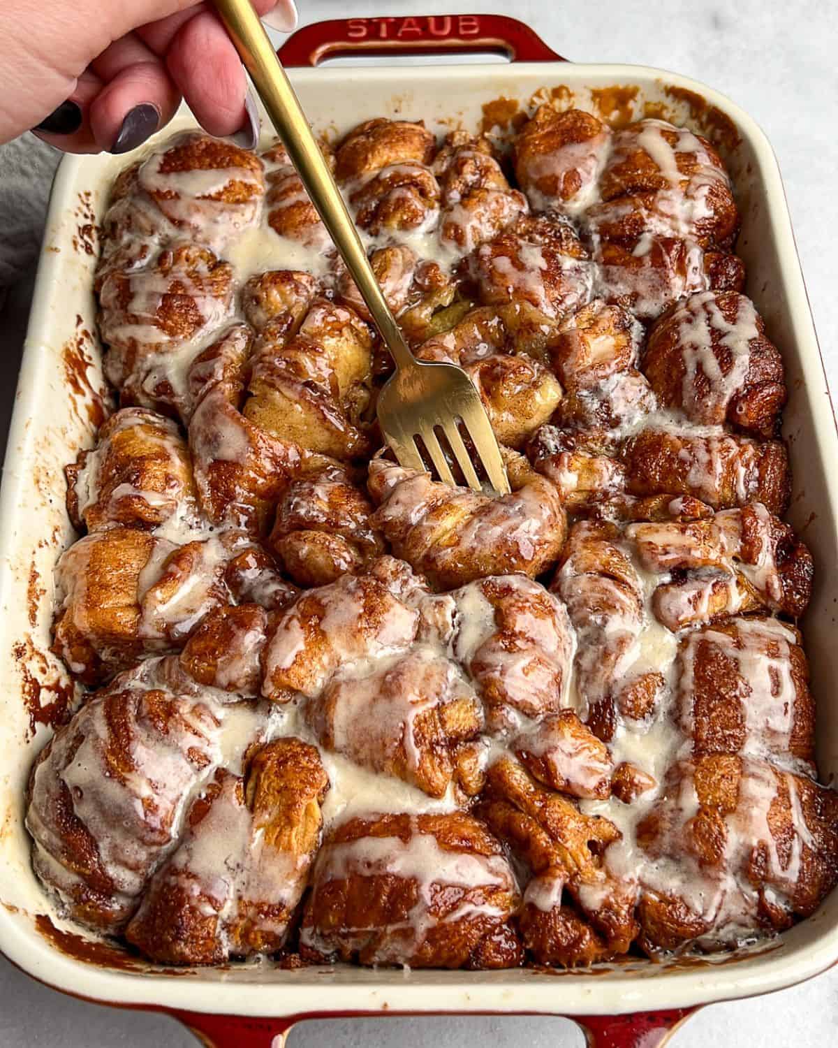 A fork diving into a baking pan of cinnamon roll bites.