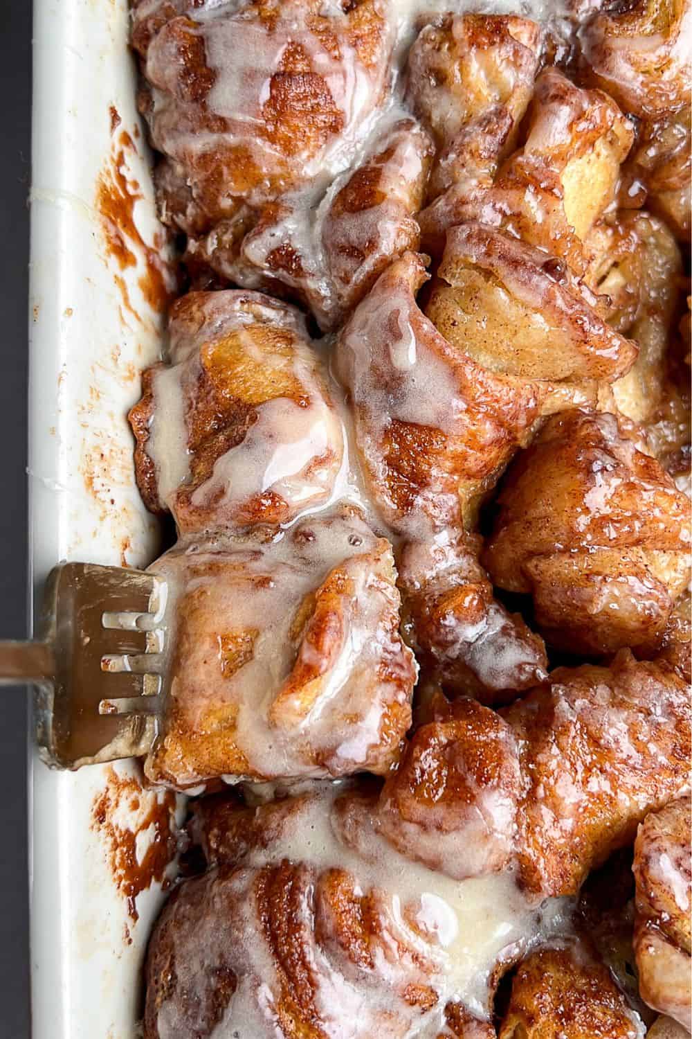 Close-up image of a fork diving into a baking pan of cinnamon roll bites.