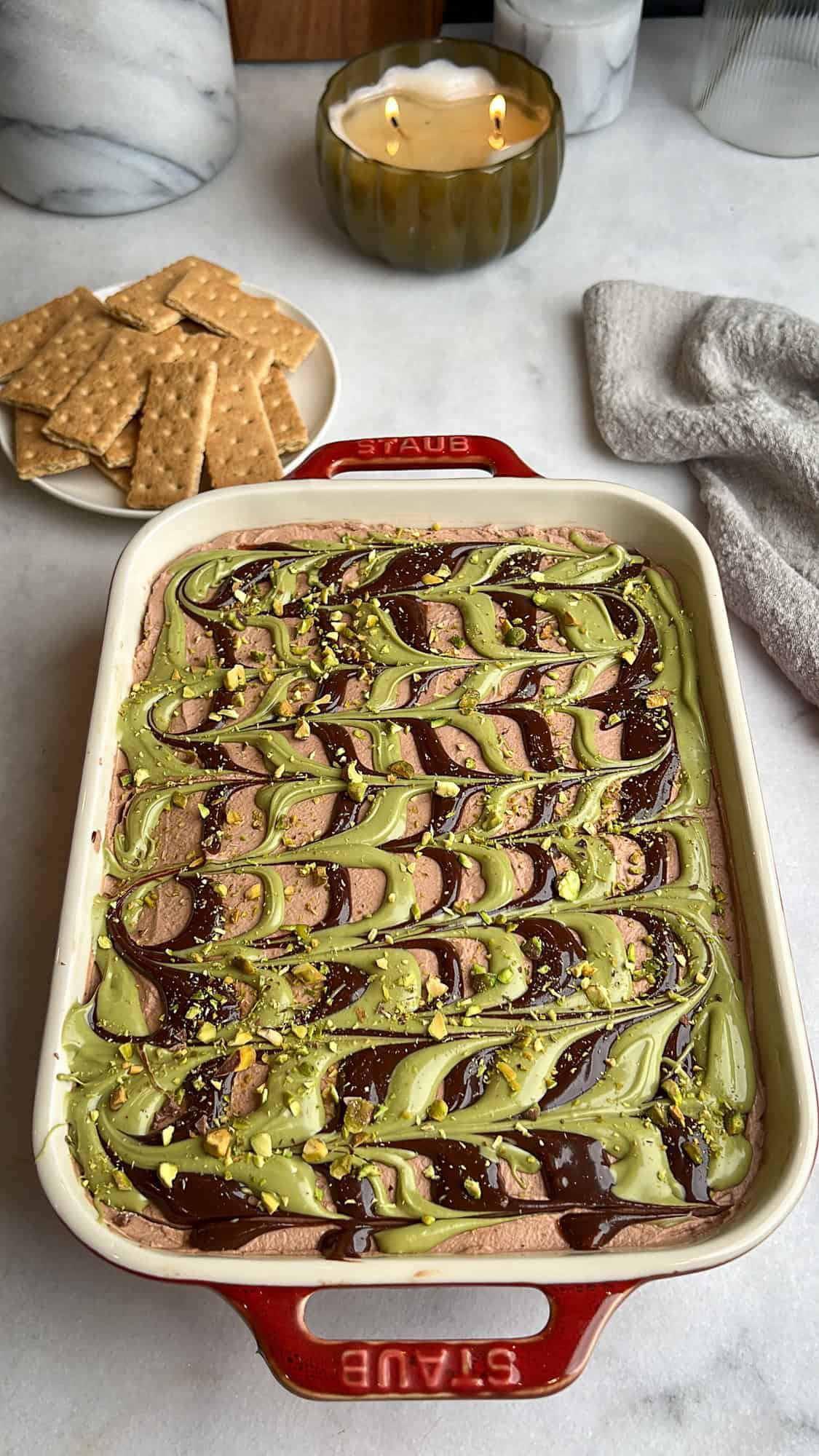 With layers of crispy kataifi, pistachio cream, and chocolate whipped cream, this Dubai chocolate cheesecake is a dream come true. Dubai chocolate cheesecake in a casserole dish near graham crackers.