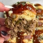 A hand holding a Philly cheesesteak slider up to the camera.