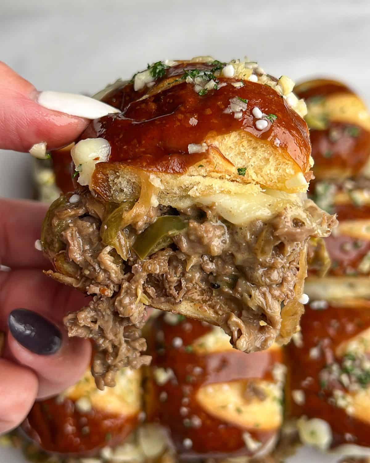 A hand holding a Philly cheesesteak slider up to the camera.
