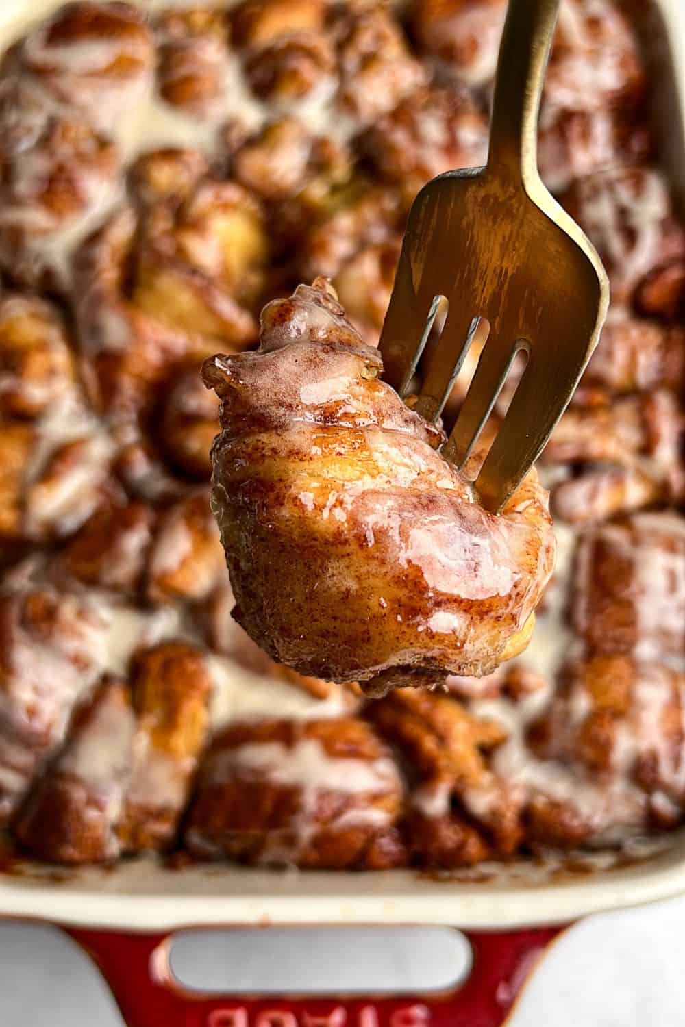 A fork holding a cinnamon roll bite up to the camera.