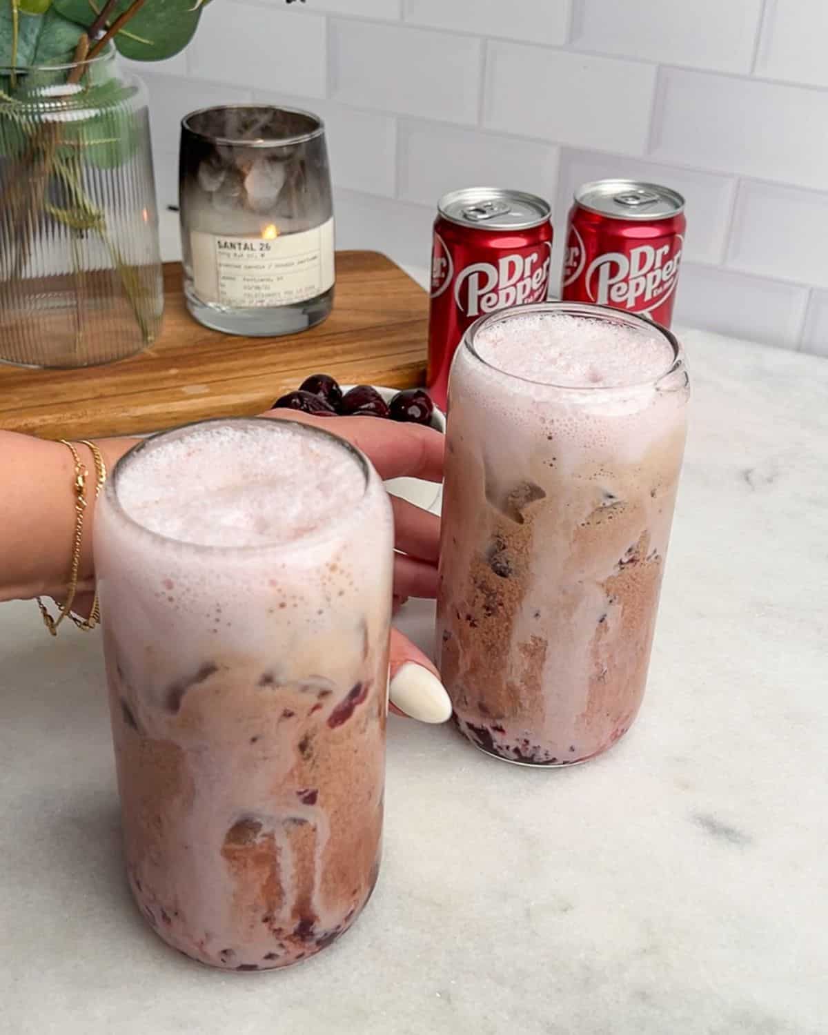 two glasses of cherry vanilla soda on a table with a hand grabbing the glass