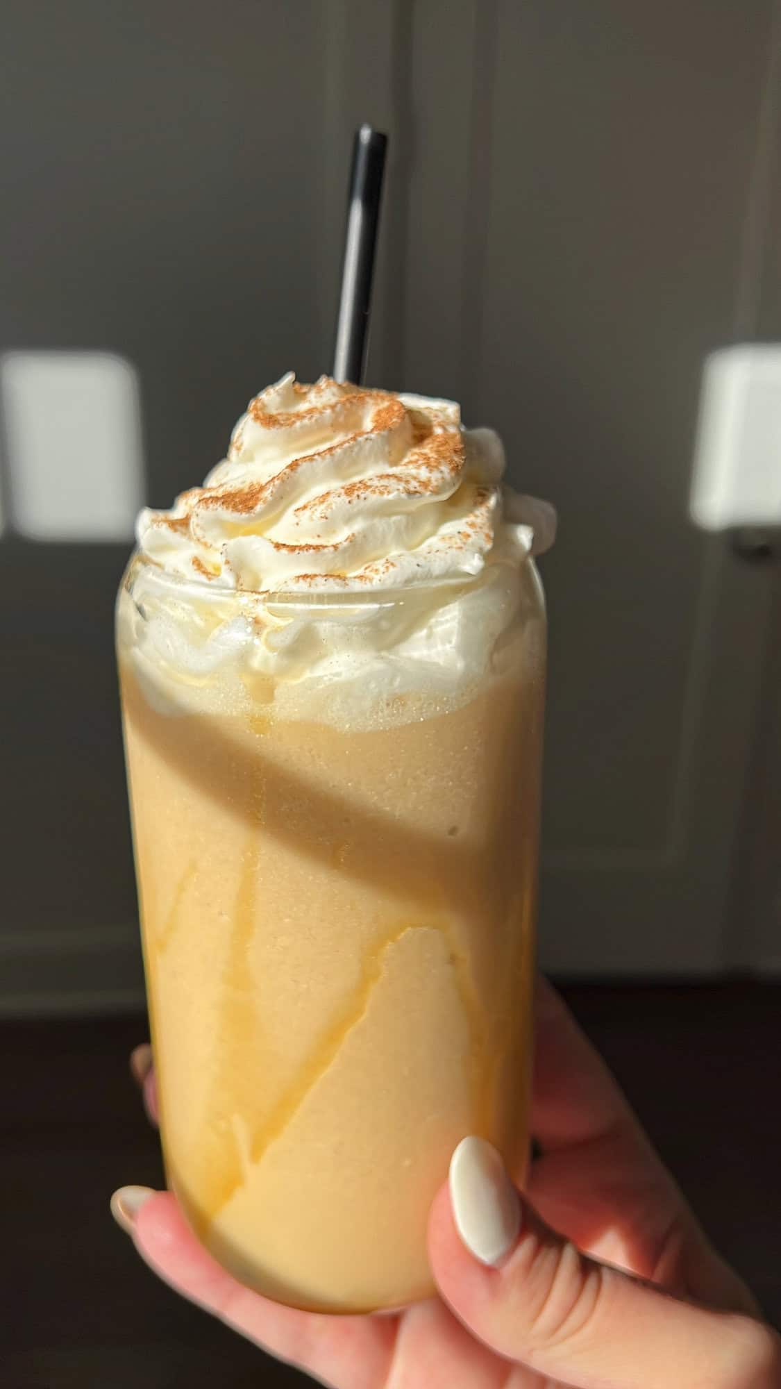 whipped caramel apple cider held in hand in the sunset