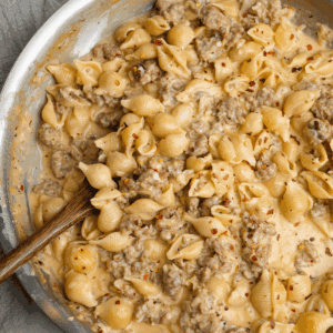 Overhead image of a wooden spoon in a skillet full of Italian sausage pasta.