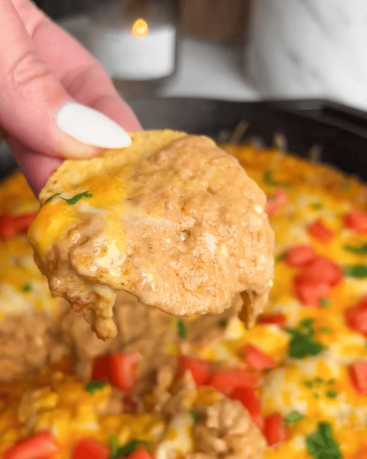 A chip holding up a scoop of cheesy refried bean dip.