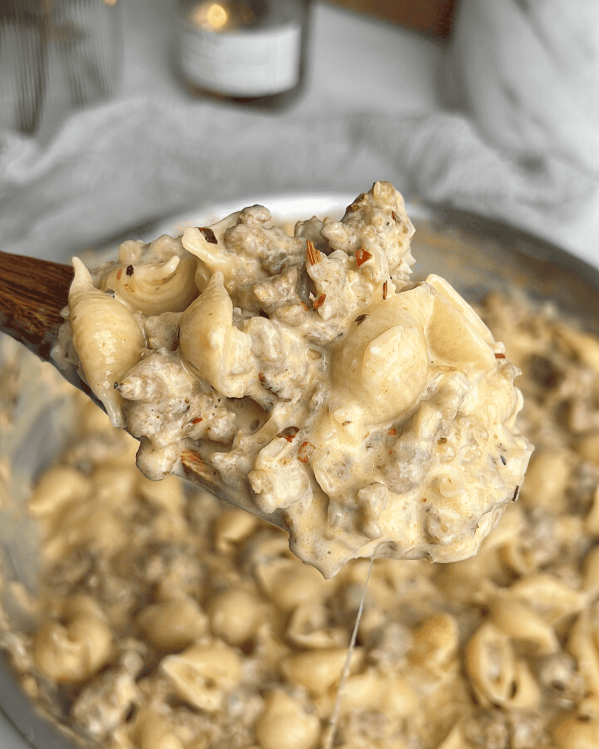 This creamy, spicy Italian sausage pasta comes together in just 30 minutes, and the luscious, cheesy white wine sauce is to die for. A wooden spoon holding a scoop of Italian sausage pasta up to the camera.