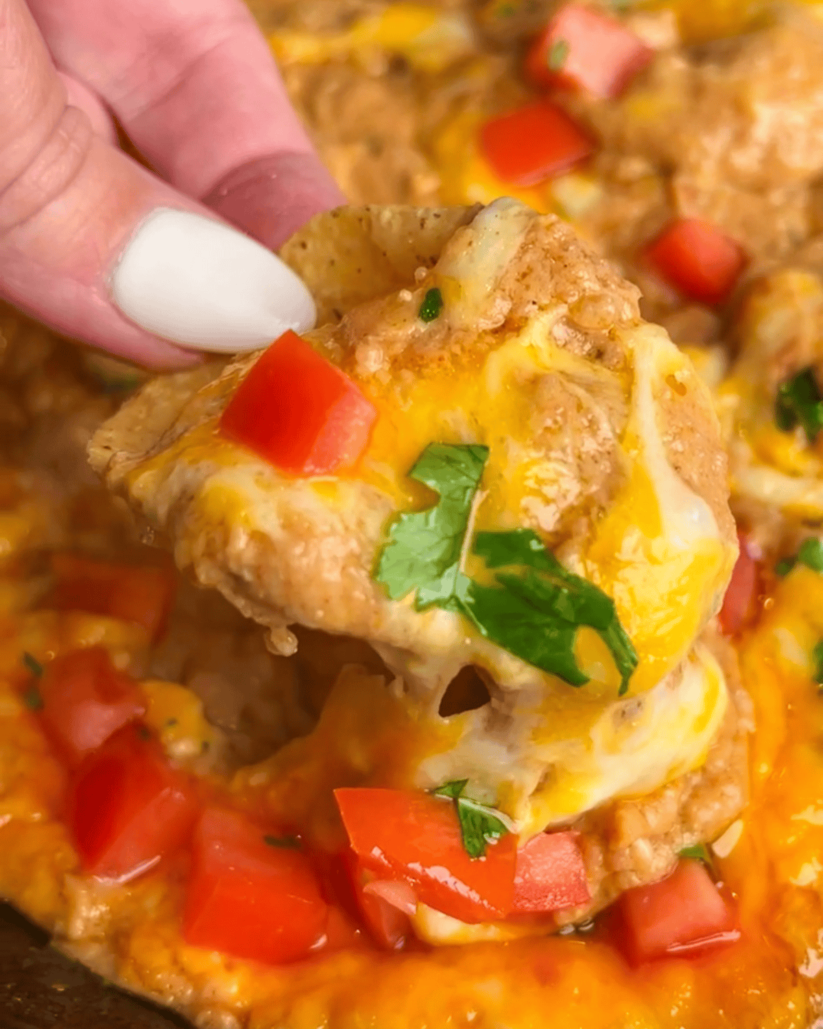 Close-up image of a chip diving into cheesy bean dip.