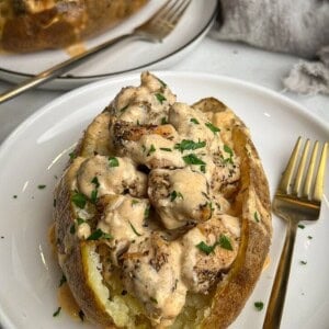 Chicken alfredo stuffed baked potatoes served on white plates.