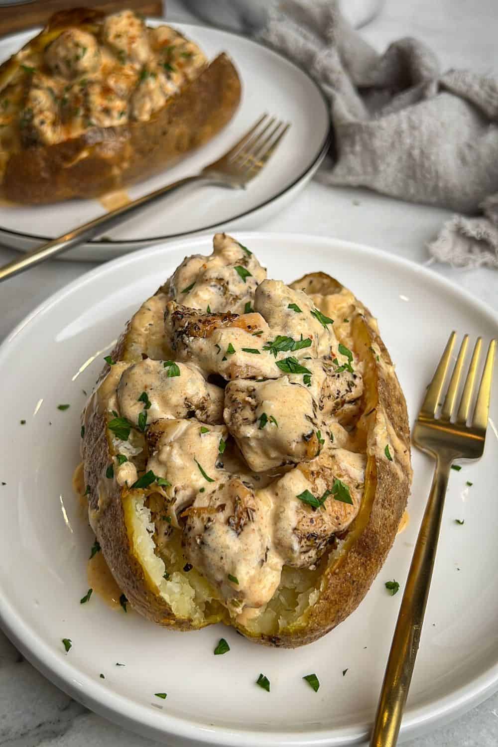 Chicken alfredo stuffed baked potatoes served on white plates.