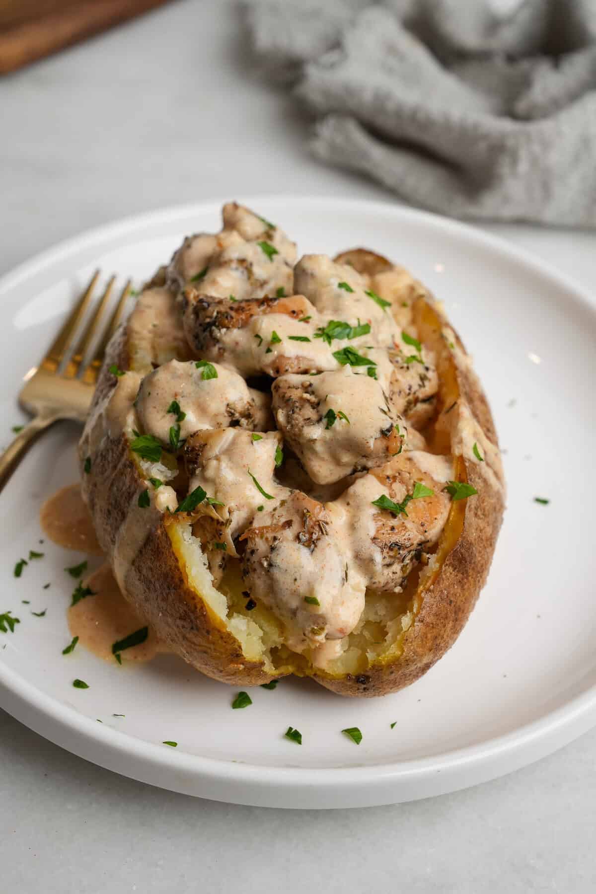A chicken alfredo stuffed baked potato on a plate.