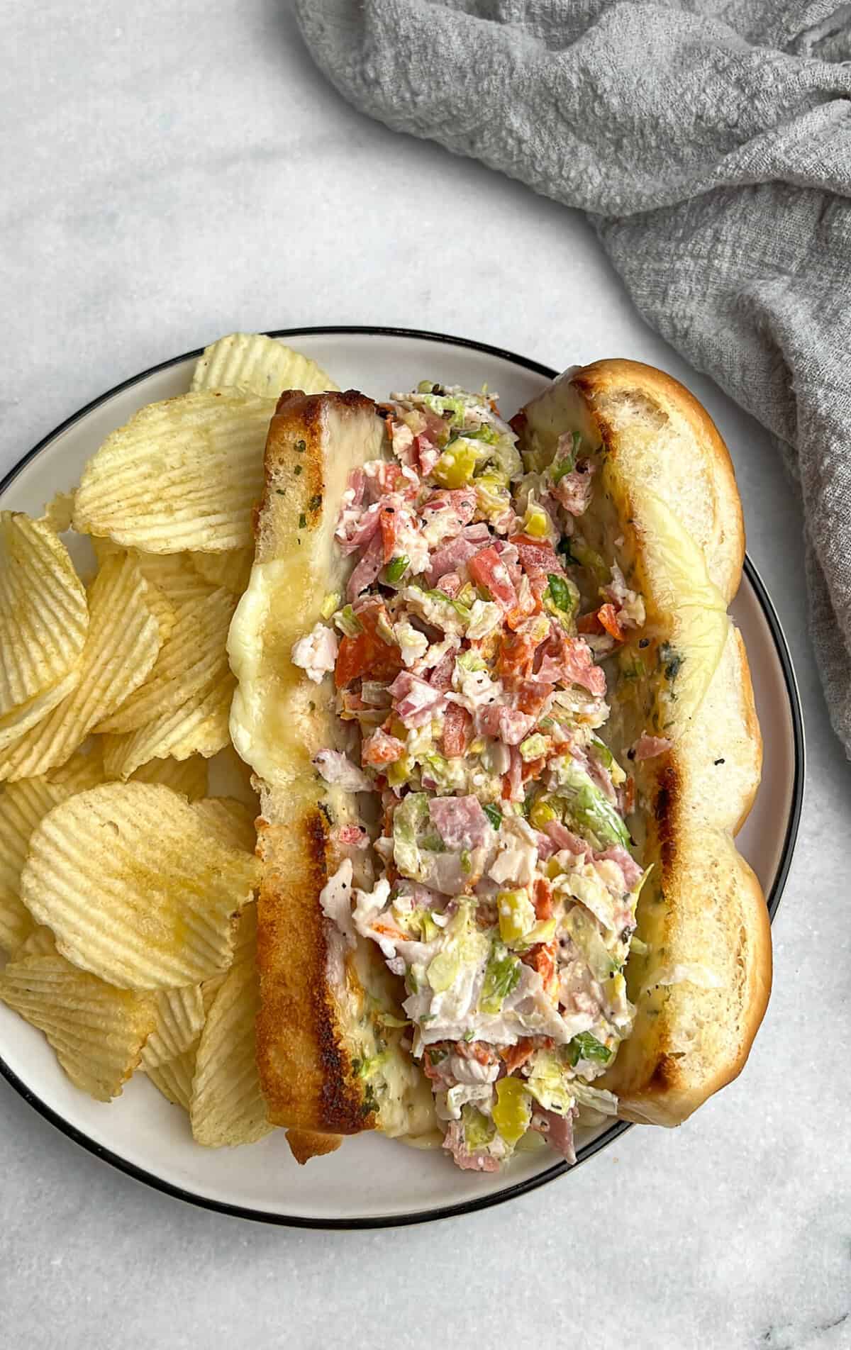 a chopped italian grinder sandwich sitting on a plate with chips