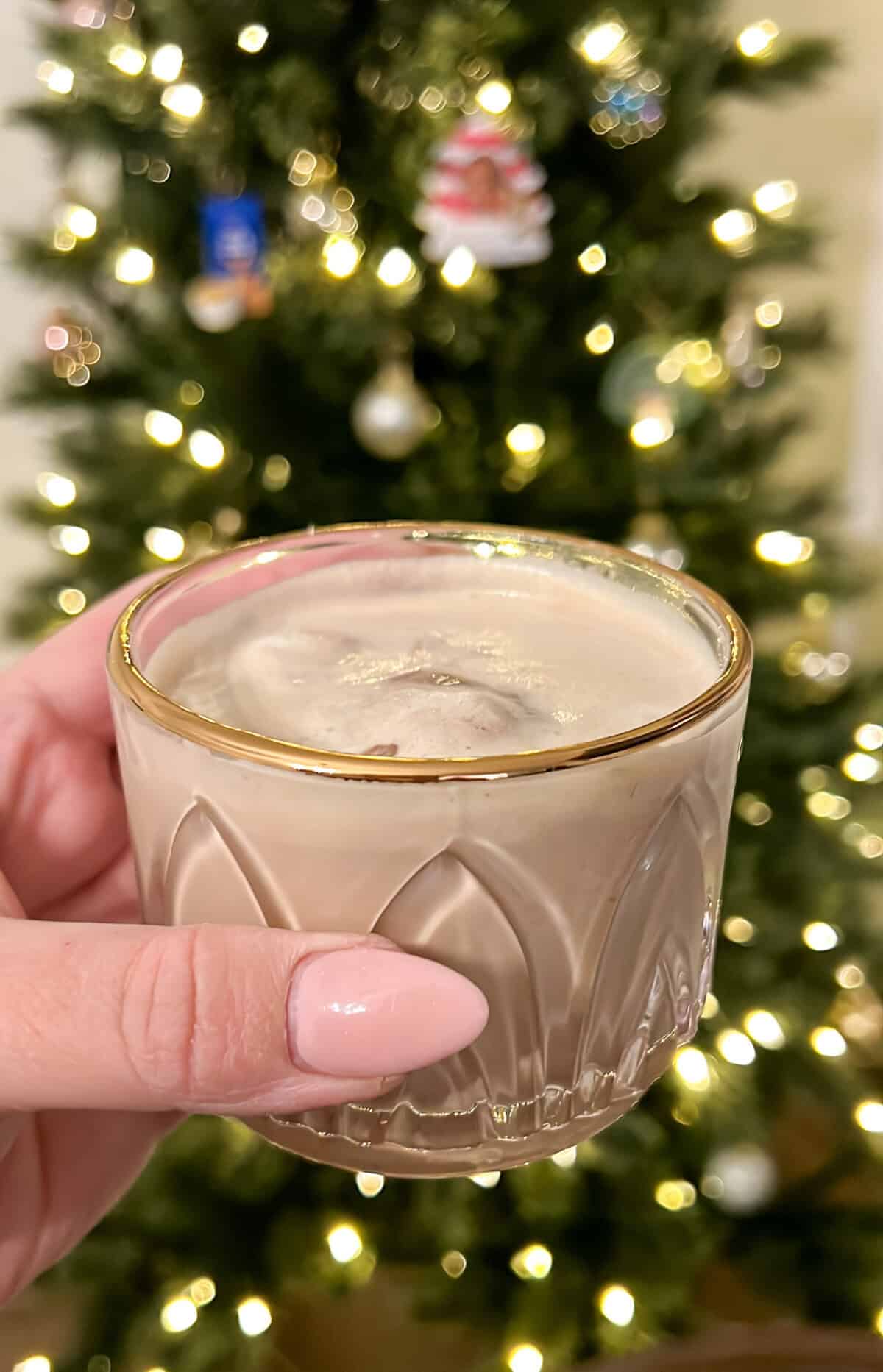 a glass with a gold rim holding a cup full of coffee punch in front of a christmas tree