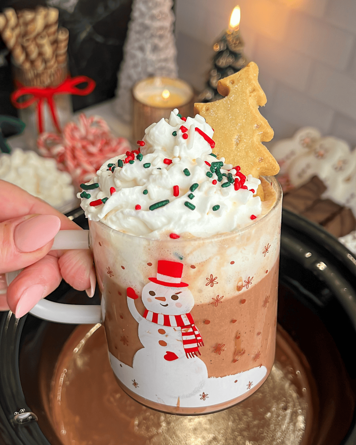a clear mug filled with crock pot hot cocoa and topped with whipped cream and christmas sprinkles.