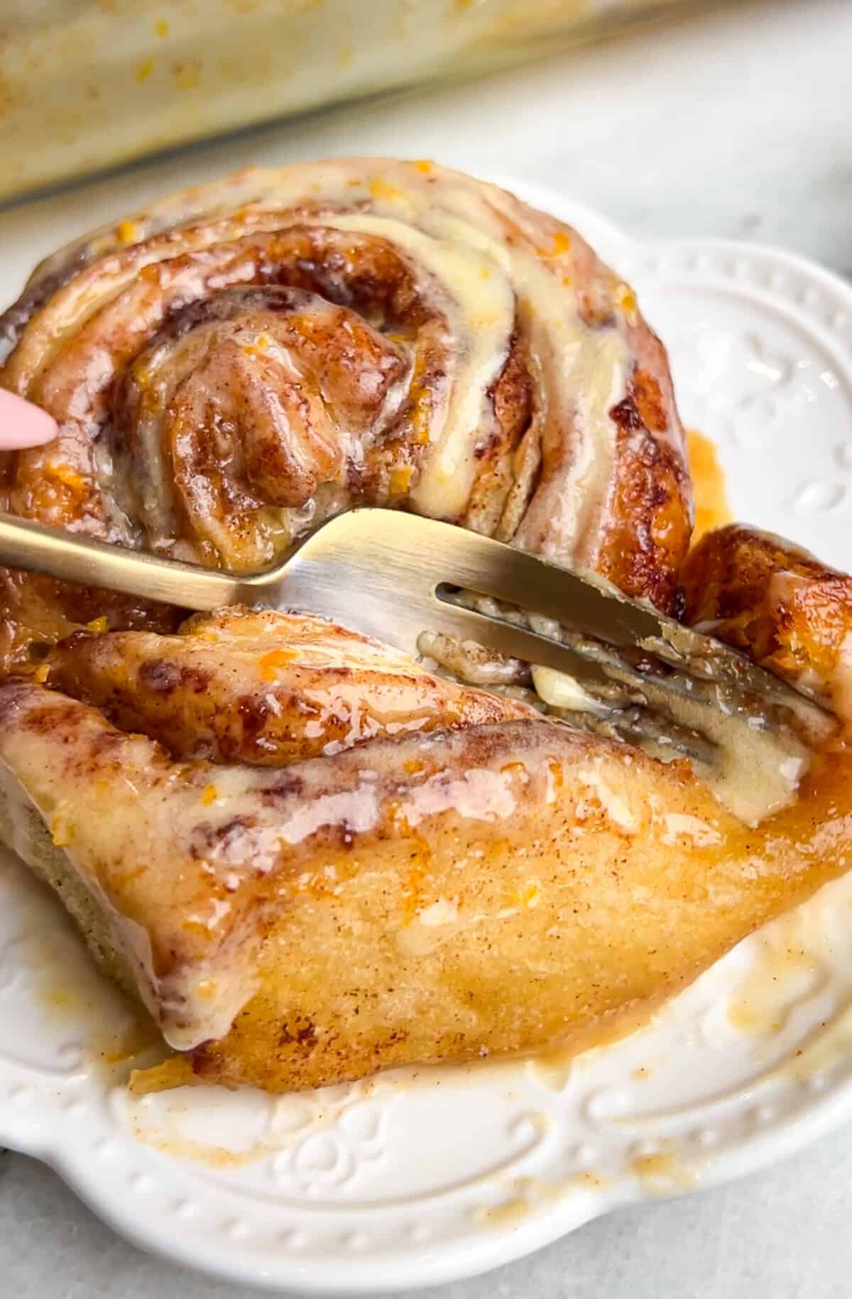 orange cinnamon roll being cut into by a fork