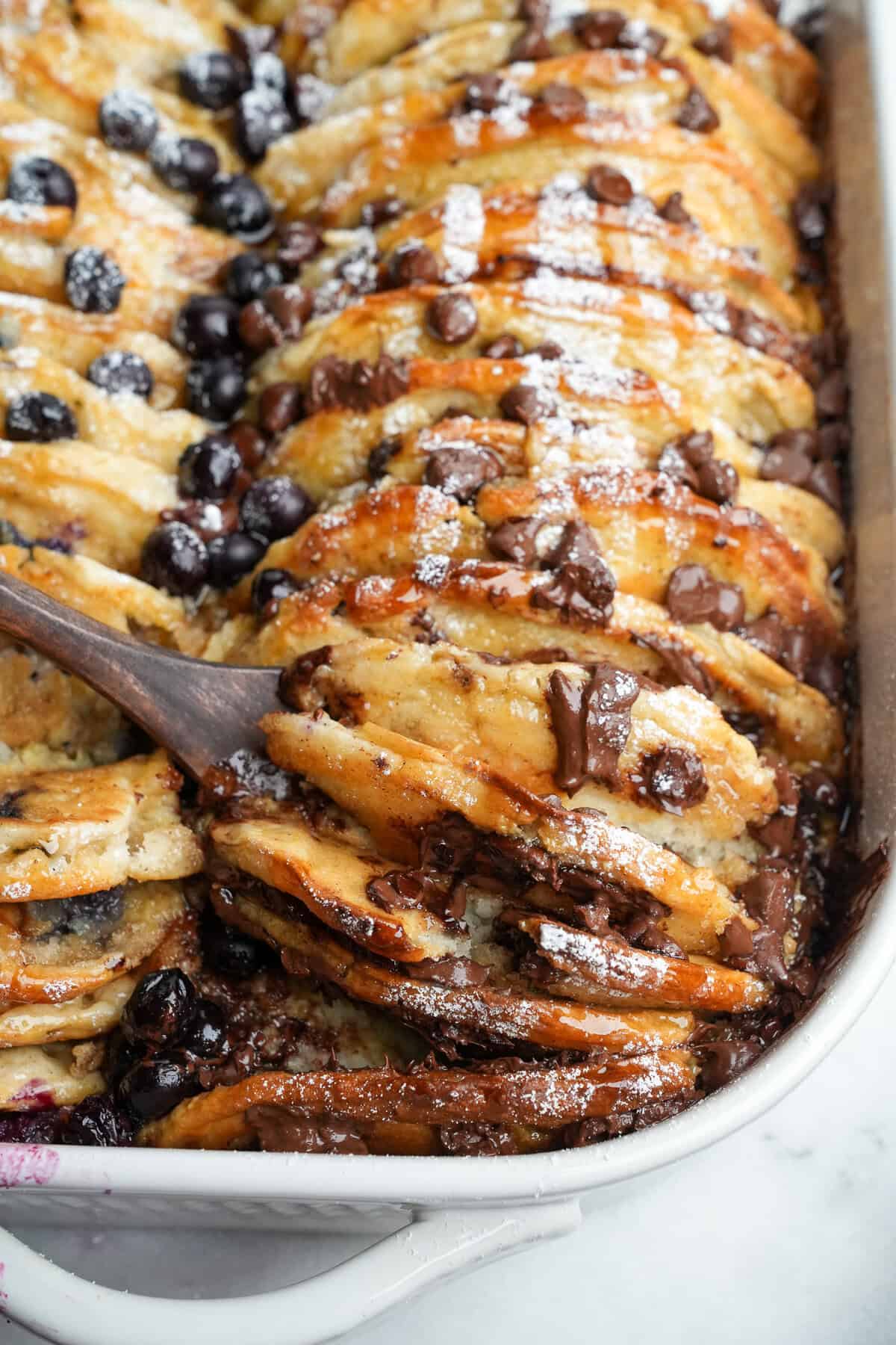 This overnight Pancake Casserole is cozy, decadent, and perfect for slow weekend mornings or holiday brunch. Super easy to make! Pancake casserole in a dish with a spoon lifting out pancakes