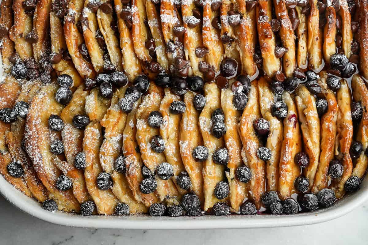 This overnight Pancake Casserole is cozy, decadent, and perfect for slow weekend mornings or holiday brunch. Super easy to make! Close overhead view of pancake casserole, half with blueberries and half with chocolate chips