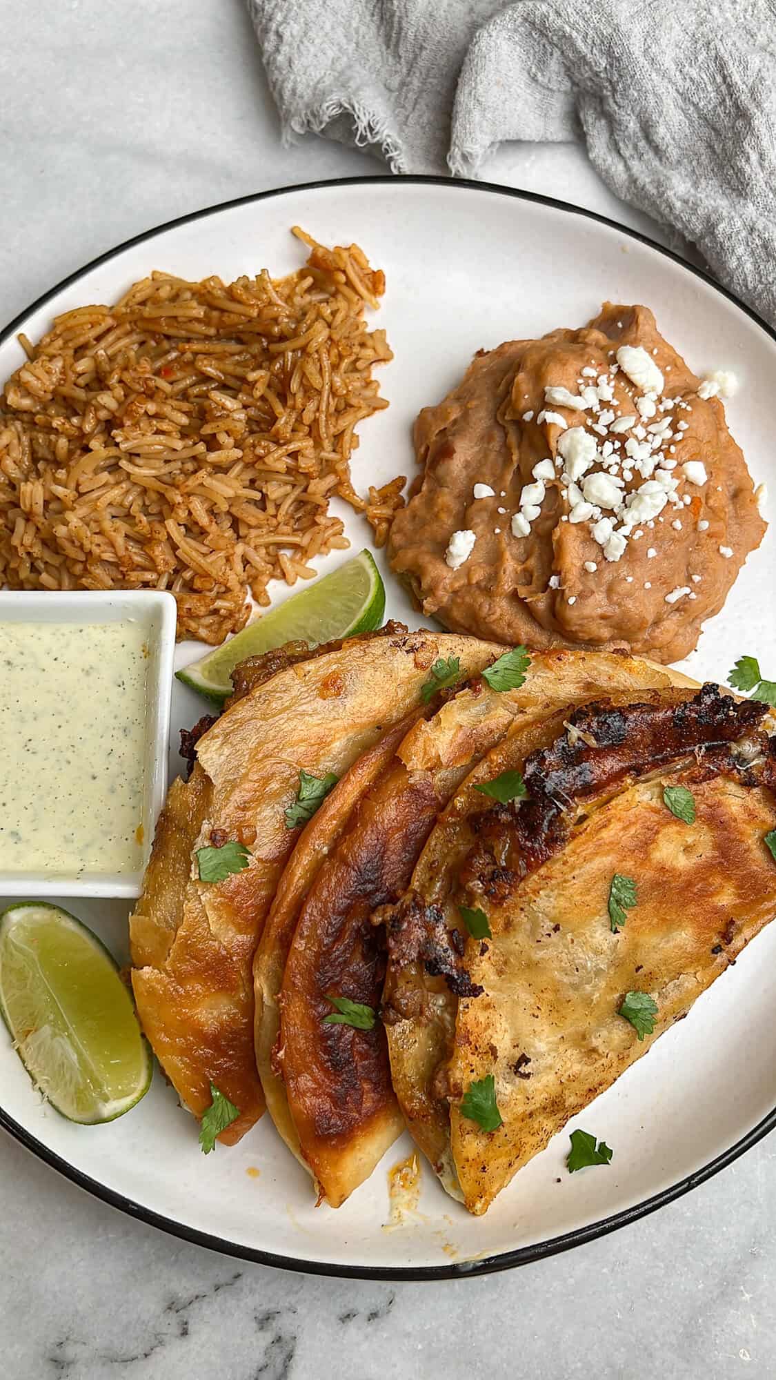 These Crispy Beef Tacos are loaded with savory, seasoned ground beef and lots of cheese, then quickly fried to crispy, melty perfection. Overhead view of crispy beef tacos on a plate with refried beans and Mexican rice