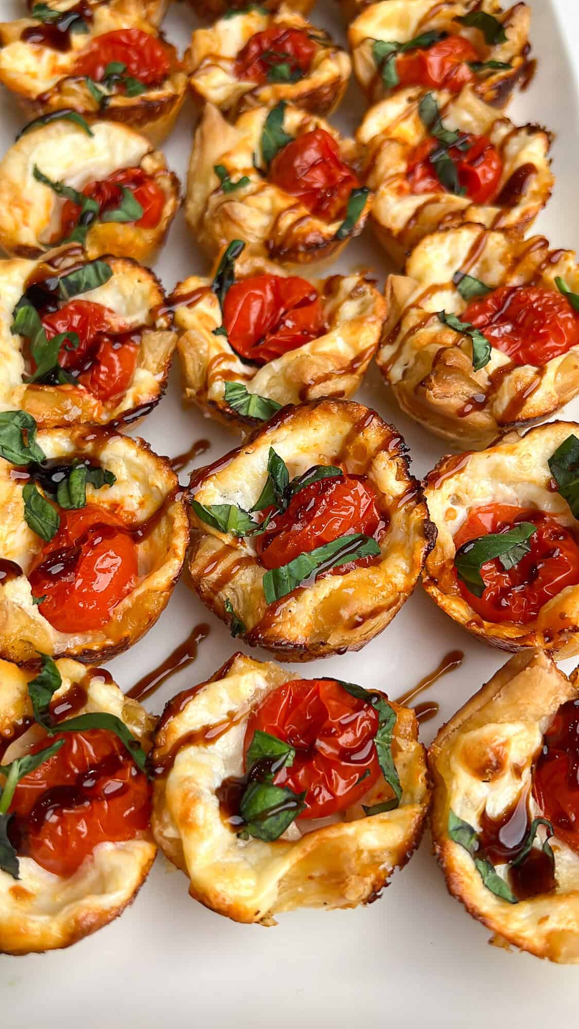 These easy caprese bites combine the fresh flavors of cherry tomatoes, mozzarella, and basil in a warm, flaky crust. Overhead view of puff pastry caprese bites on the countertop
