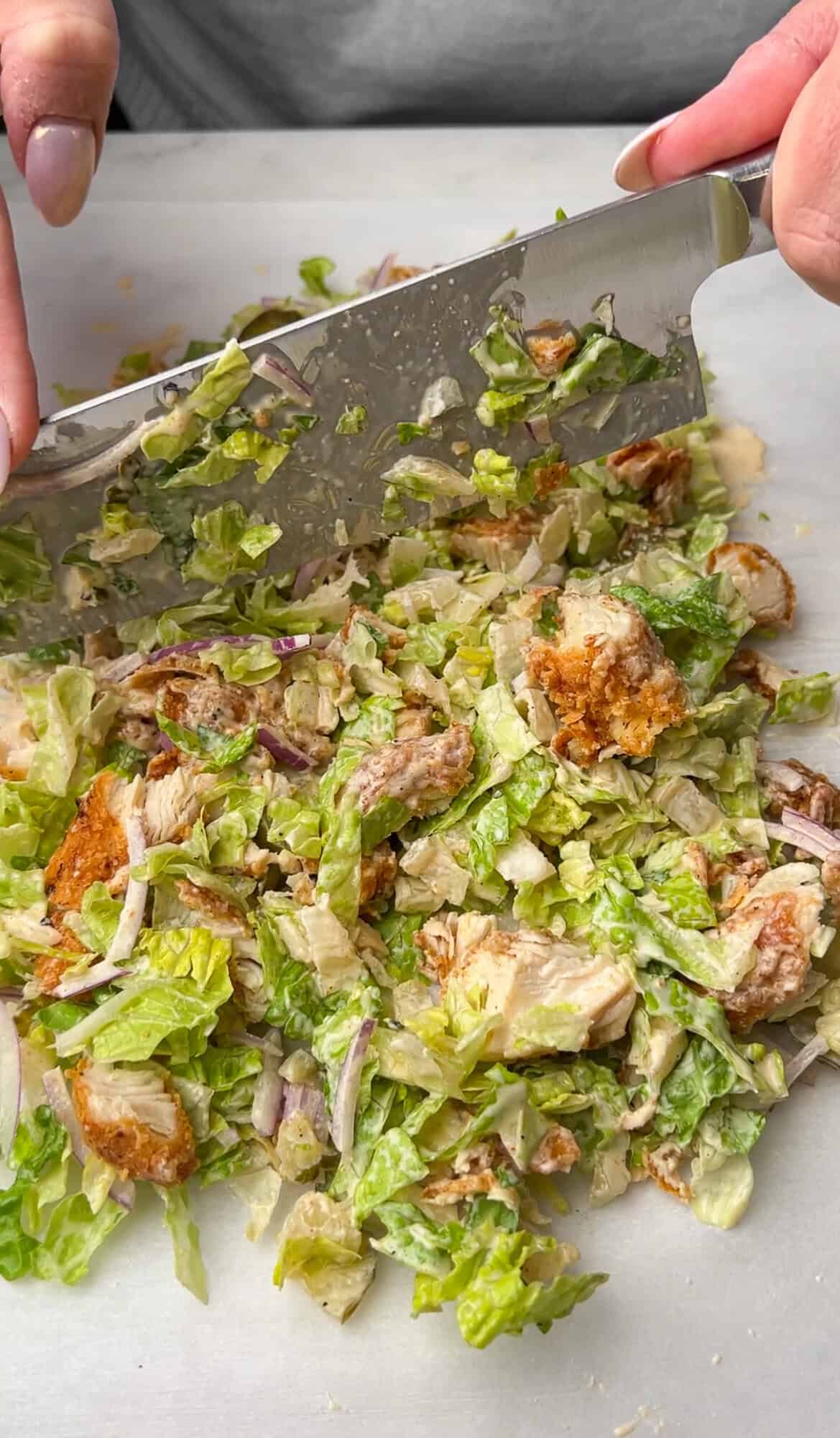 chopped chicken sandwich ingredients on a cutting board being chopped with a knife