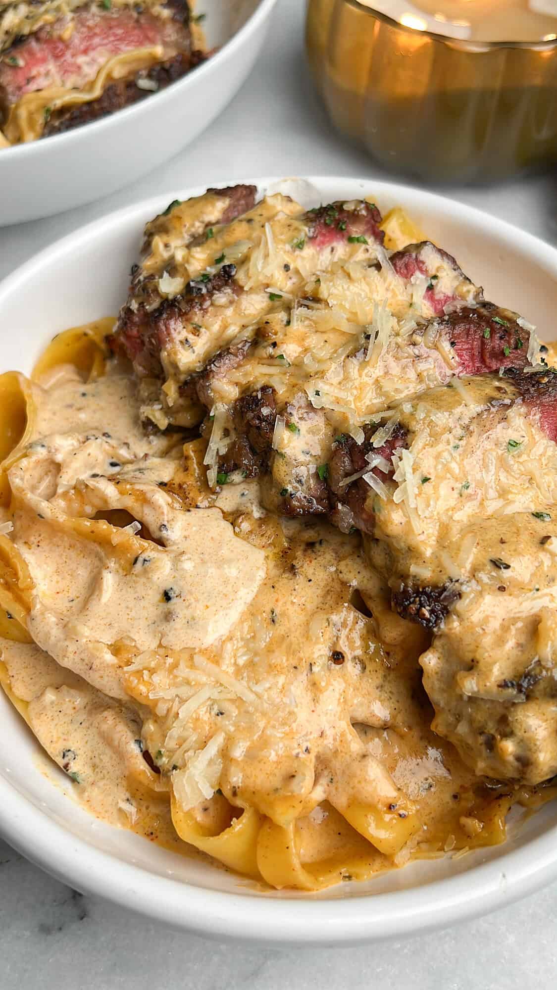 steak with poured cream sauce on top sitting on pasta in a bowl
