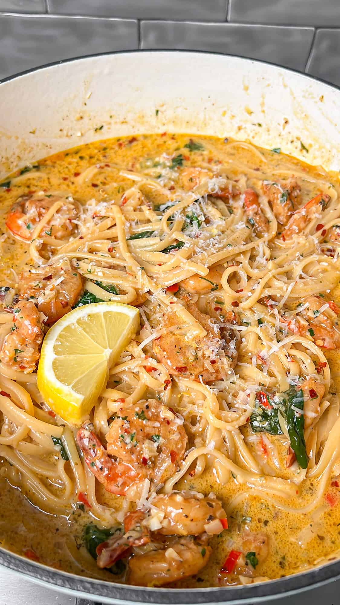 cooked shrimp scampi in a pot with lemon wedges